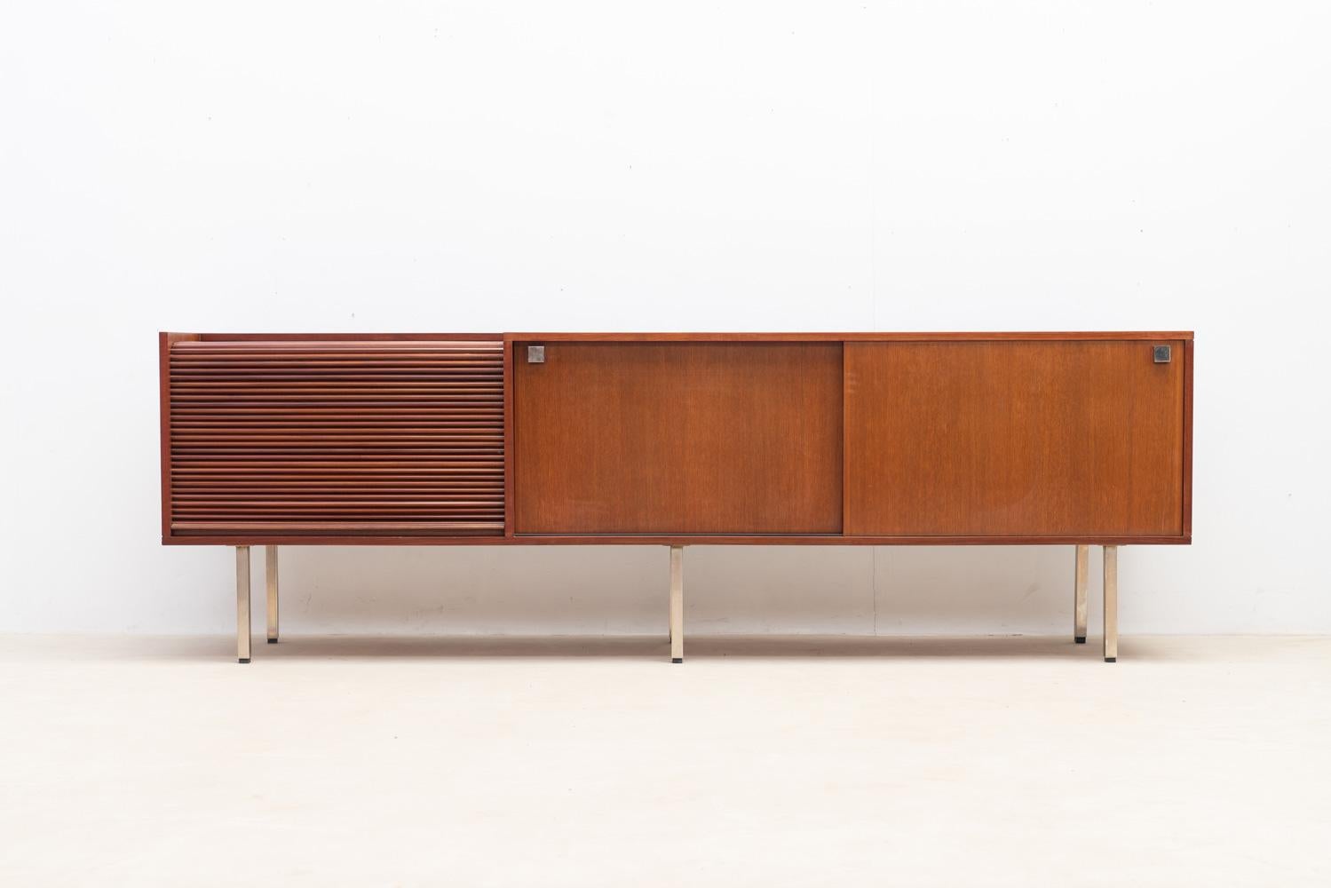 Entrez dans les années 1960 avec ce rare buffet Belform, conçu par le designer belge Alfred Hendrickx. Doté d'une porte qui roule horizontalement sur la gauche, il cache un mini bar avec un plateau en verre et un tiroir. Le côté droit présente des