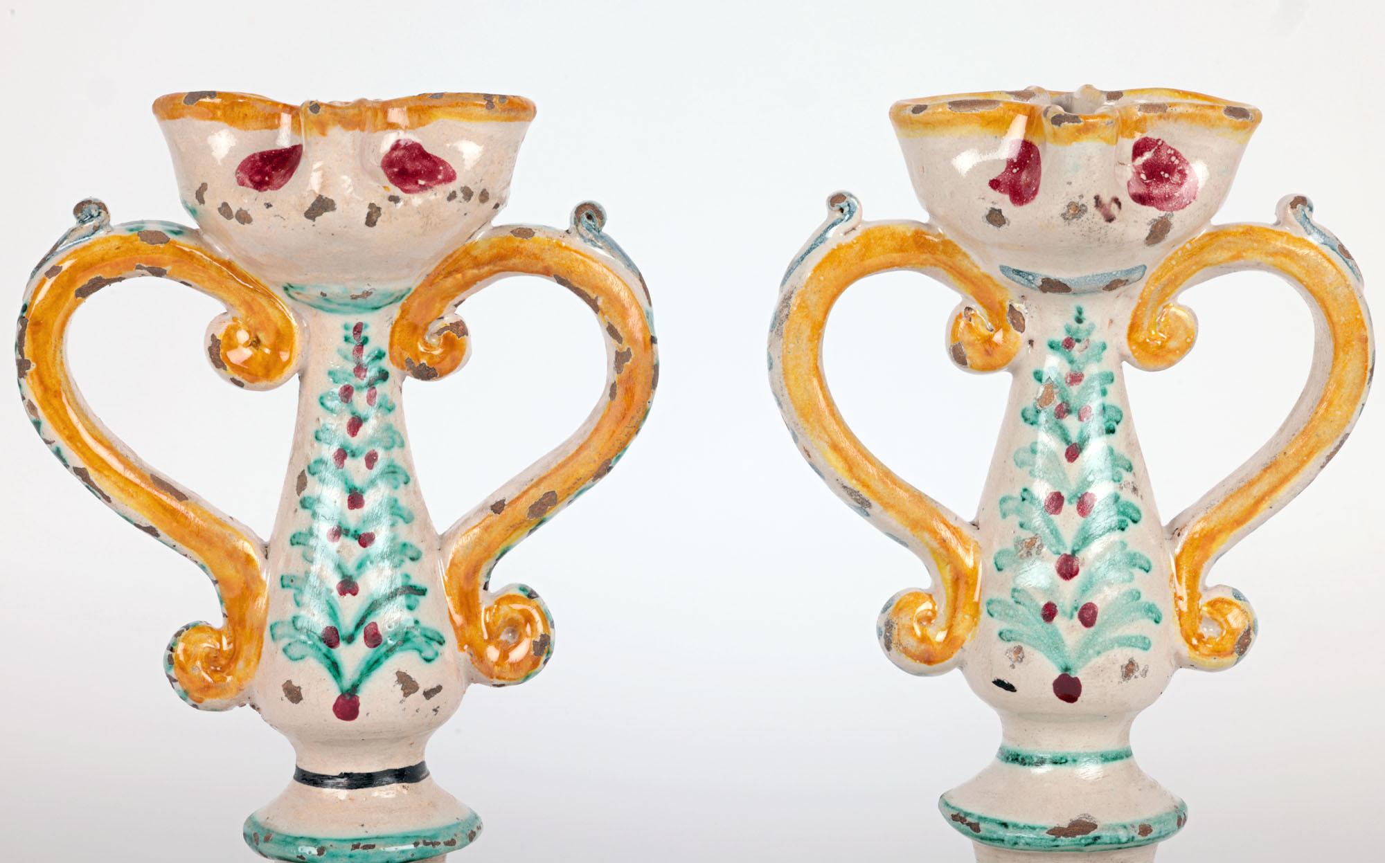A stylish pair antique South Italian Sicilian maiolica pottery twin handled candlesticks dating from the 18th century. The handmade earthenware candlesticks stand on a wide bowl-shaped foot with a flat partially glazed base with upright sides. The