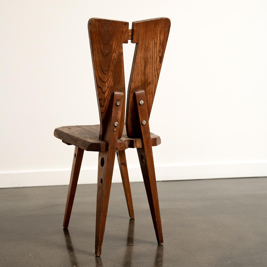 Dieser französische Beistellstuhl im Stil von Christian Durupt und Charlotte Perriand zeichnet sich durch eine kühne, kantige Silhouette und eine warme Patina aus, die auf seine handwerklichen Ursprünge verweisen. Die geteilte Rückenlehne und die