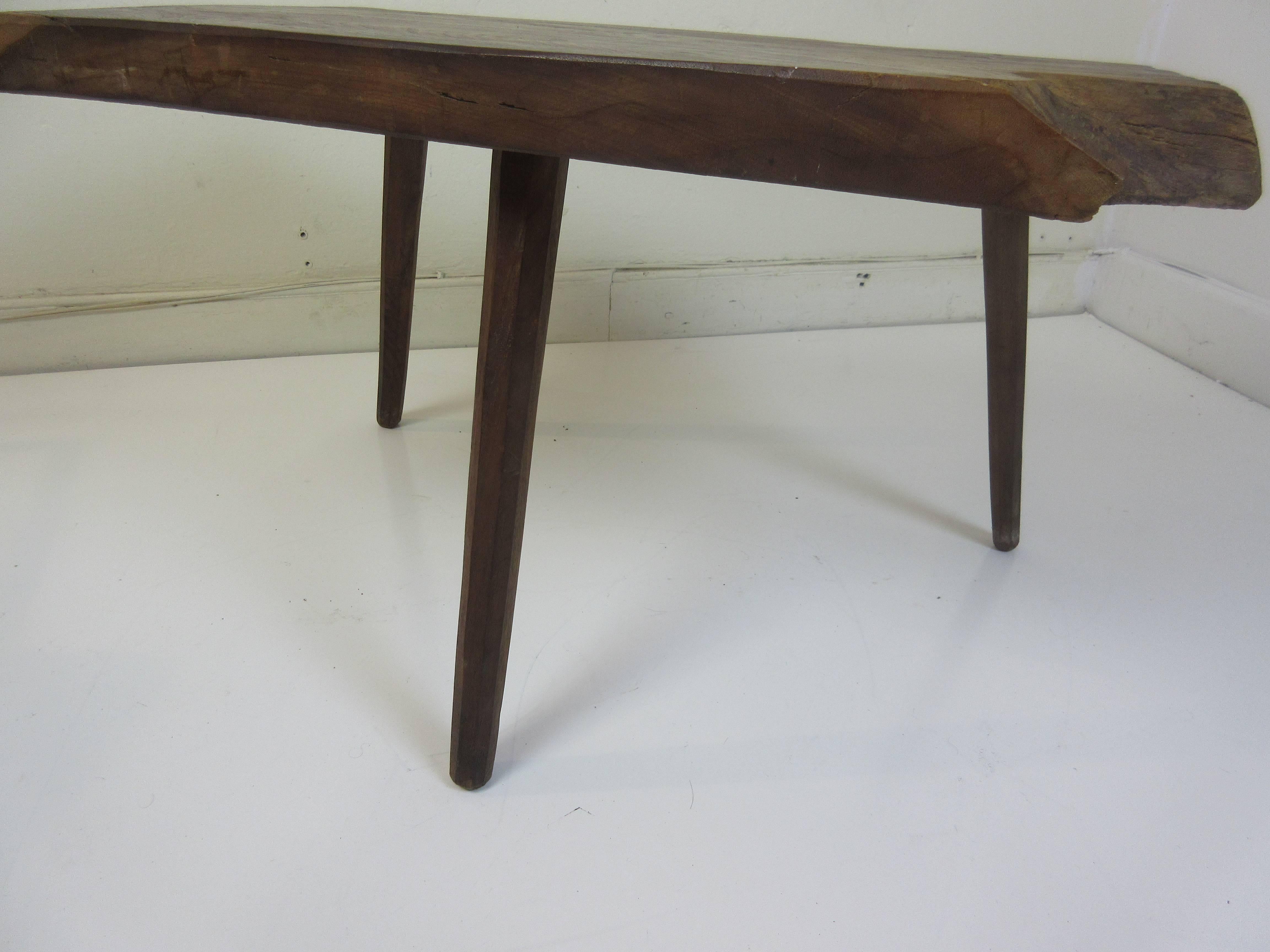 Side or coffee table in the style of Nakashima with a date of 1973 carved on the underside. Rough natural edged top with three angled legs with faceted sides.