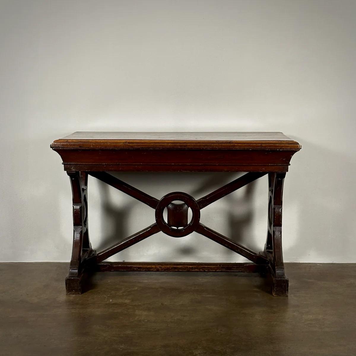 19th-century English X-frame table, distinctively styled with a painted finish that highlights its armorial crest detail. This table is characterized by its robust structural design and decorative appeal, featuring a crossed-leg support which adds