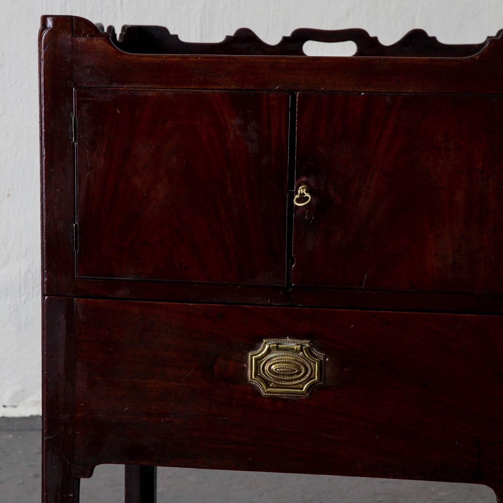 A side table or nightstand made in mahogany with brass hardware. One shelf and a drawer for storage. England 1700s during the Georgian period.