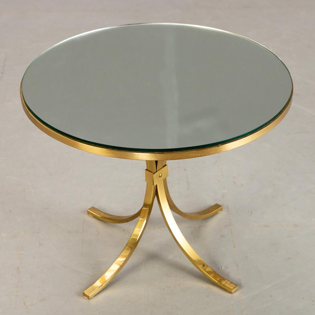 The low brass side table dating from the 1960s is an elegant piece of furniture that captures the essence of retro design and sophistication of the era. With its beautiful curved legs and a glass top, this table fuses the resistance of brass with
