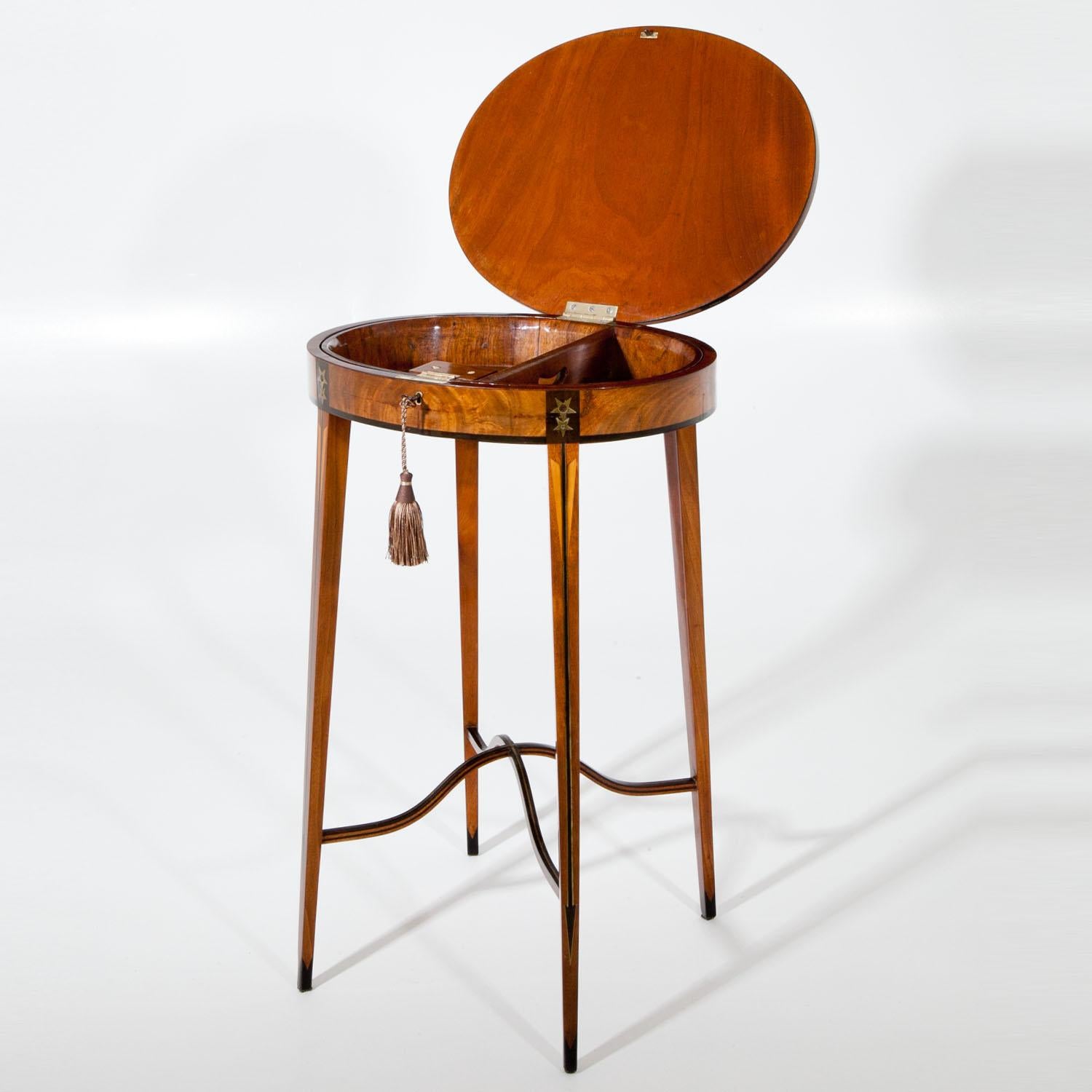 Small side table, standing on long slender tapered legs with crossed and curved strutting in between. The oval body is decorated with star-shaped inlays, the legs show arrows. The interior holds a removable tray and the lid is stamped CHAPUIS.