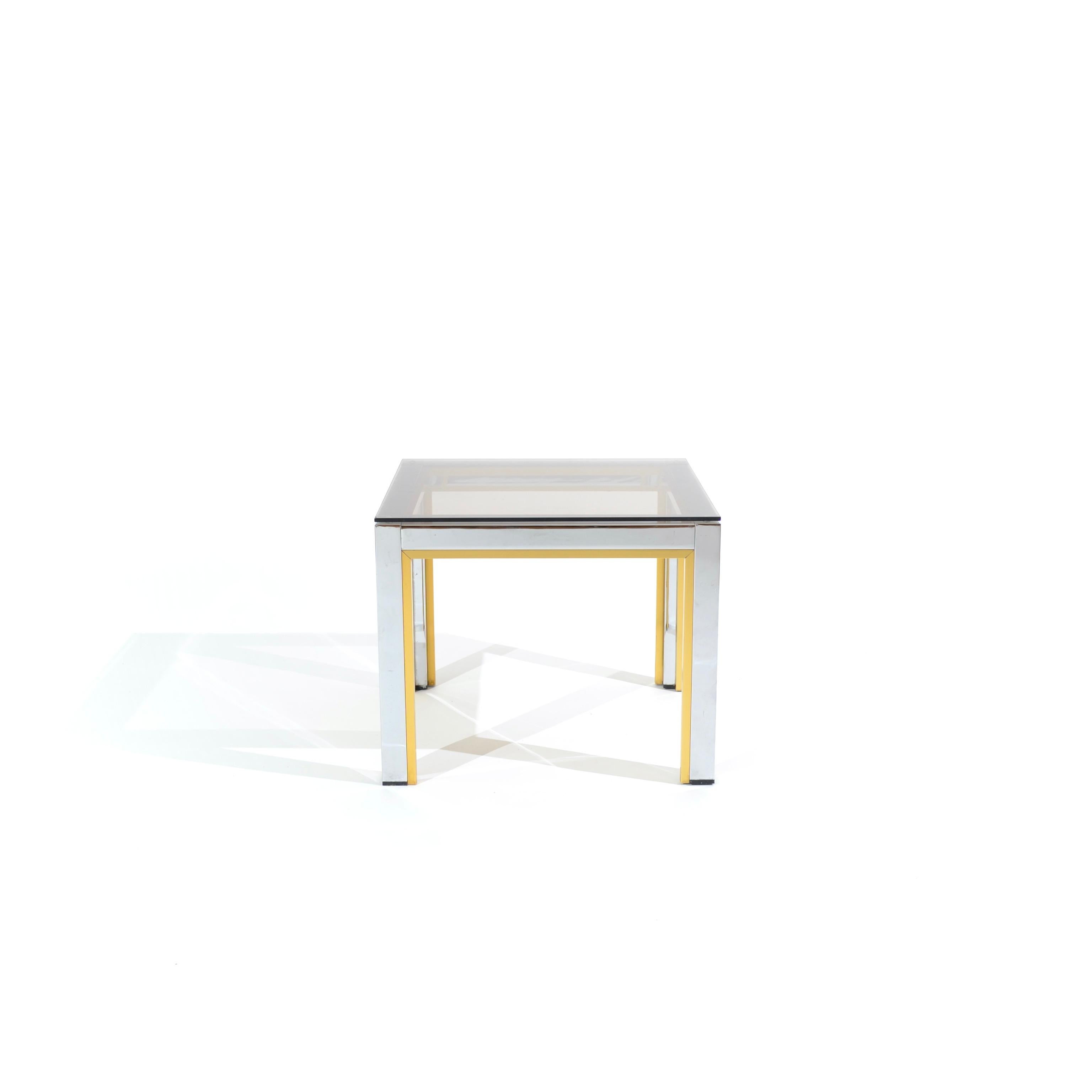 Discreet in size and elegant in style. This side table straight out of the 70's, casually combines chrome, brass and smoked glass in a humble cubic format to delight lovers of Italian design.