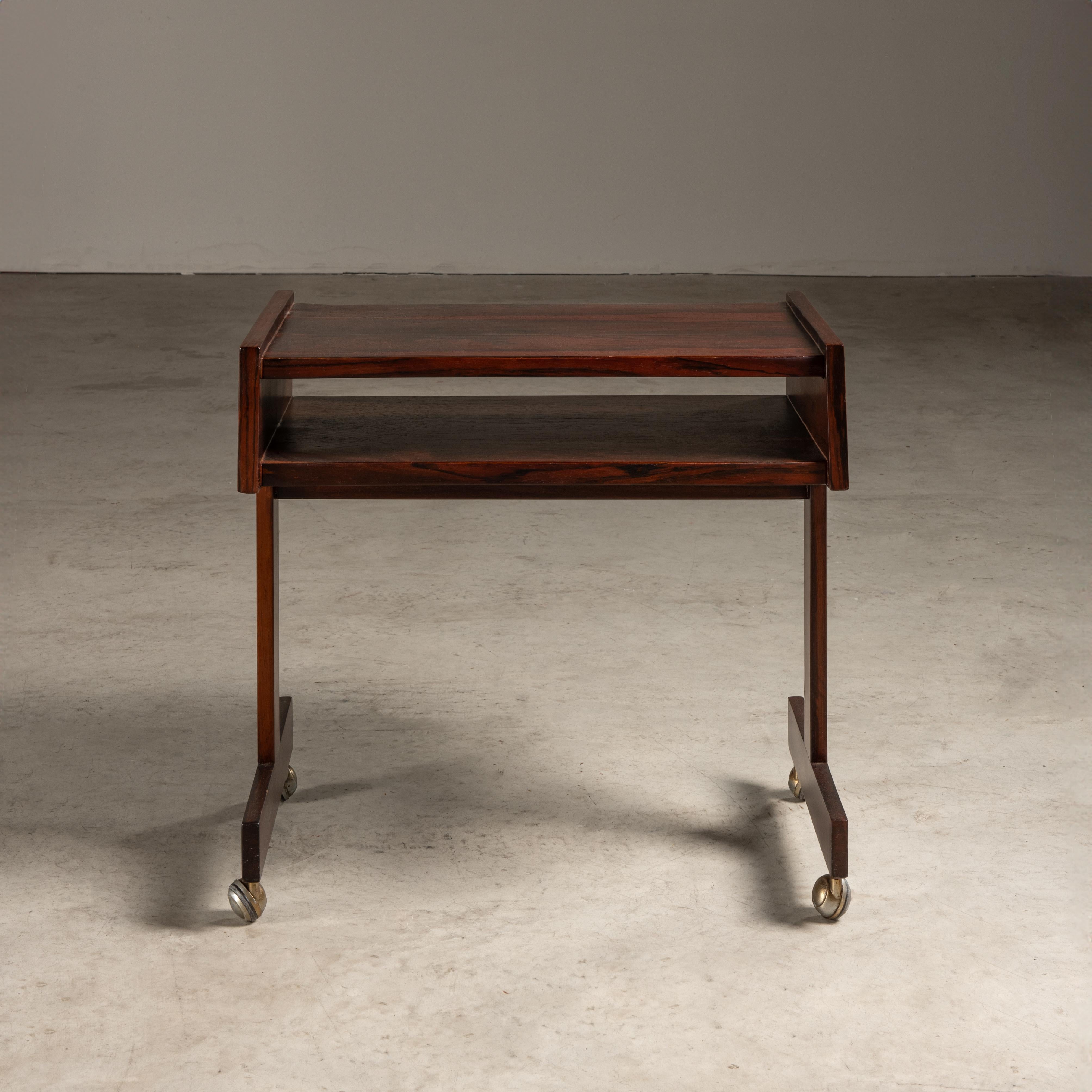 This side table by Sergio Rodrigues is a quintessential piece of mid-century Brazilian furniture design, which combines elegance with practical functionality.

The table features a rich, dark wood construction in Brazilian hardwood, which was