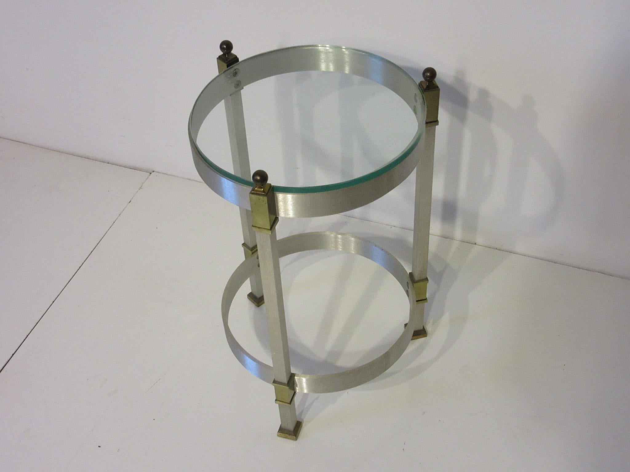 A brushed aluminum, brass detailed plate glass topped round side table or cigarette table, well constructed and the perfect size for that lounge chair or smaller space. Designed in the manner of Maison Jansen.
