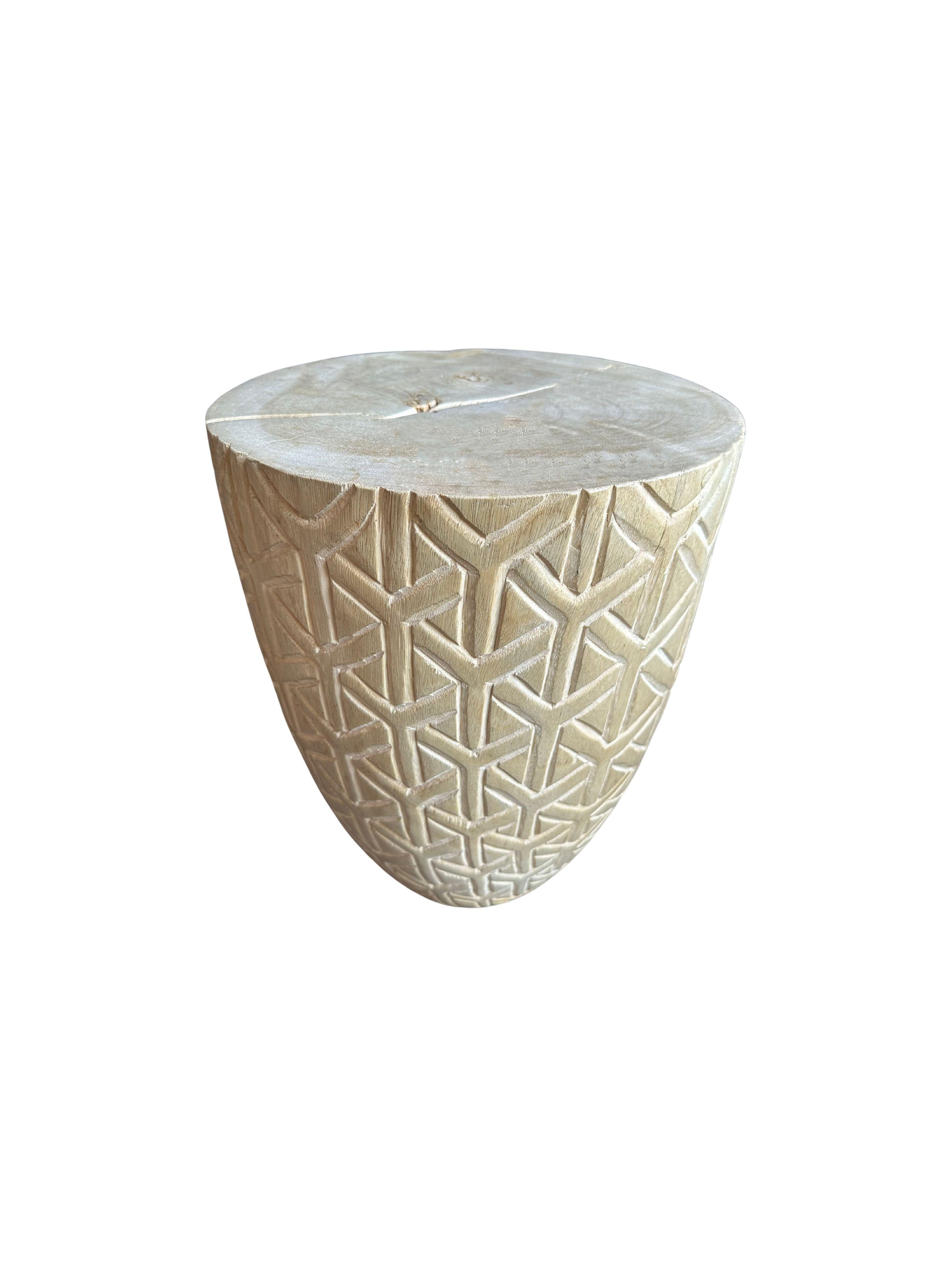A wonderfully sculptural side table with a geometric pattern hand-carved on all sides. Its pigment was achieved through bleaching the wood. Its neutral pigment and subtle wood texture makes it perfect for any space. . This table was crafted from