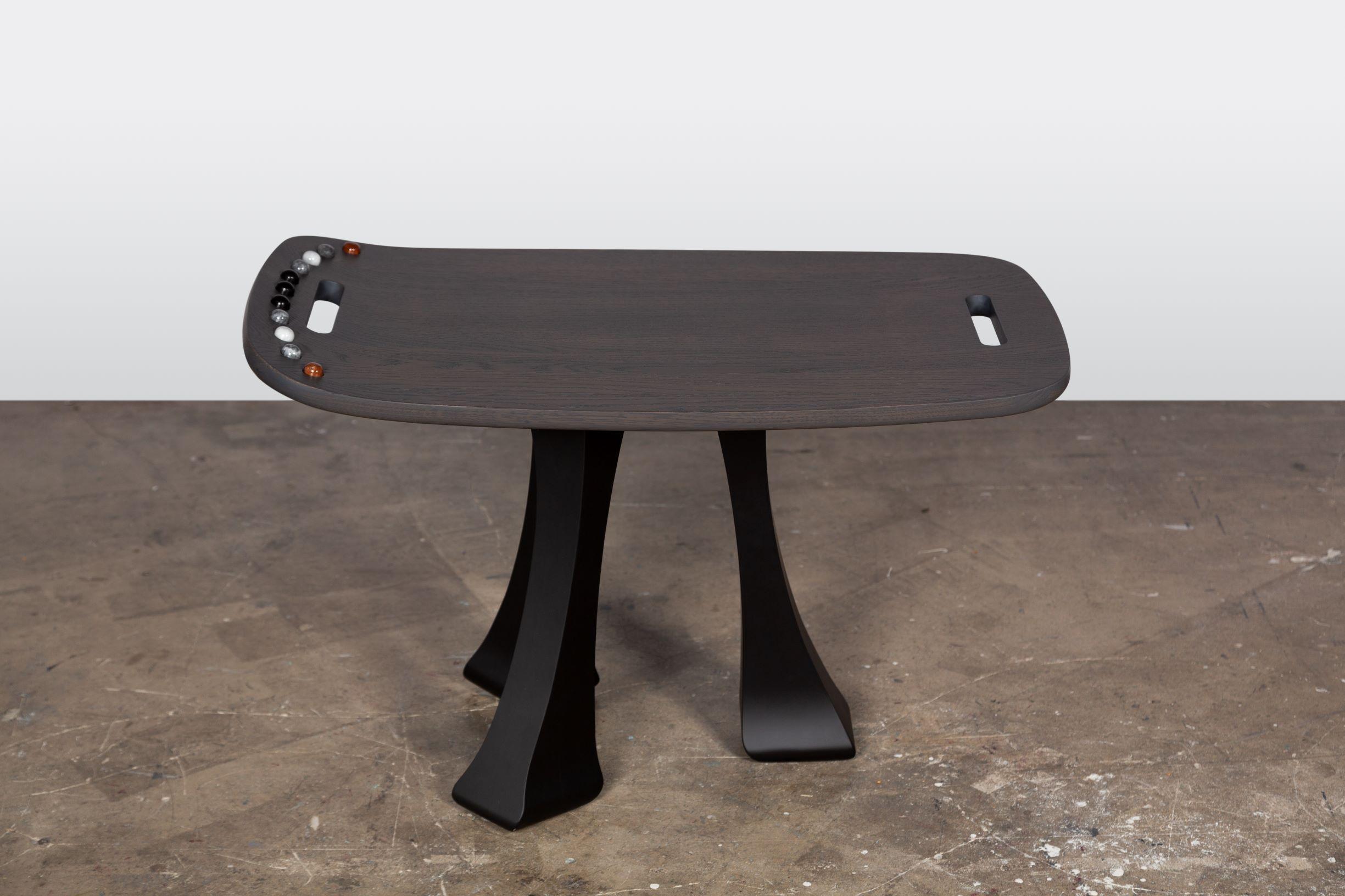 The side table from the SoShiro Pok collection is hand carved in Italy from solid oak, finished in turtle dove grey, and embellished with inlaid polished marble gems. This ergonomic wooden 3-legged coffee table has an elegant upward curve with a