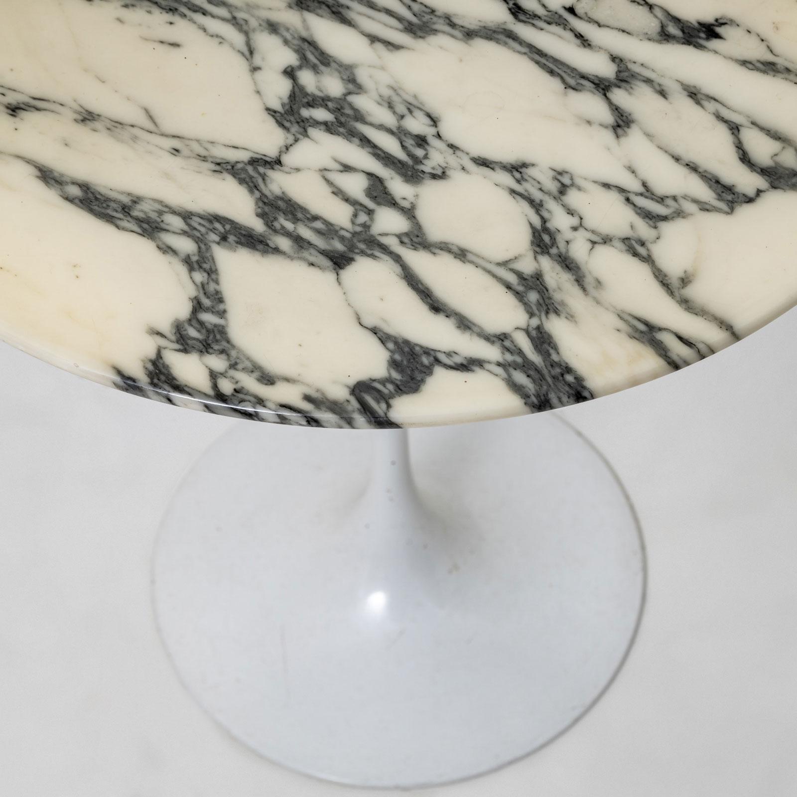 An elegant side table in the style of the iconic Tulip Table by Eero Saarinen. The table features a trumpet-shaped base with a white lacquered finish and a round tabletop made of white marble with striking black veining. A timeless design piece that