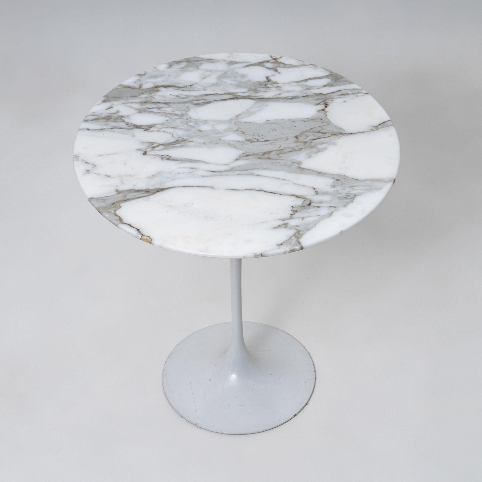 An elegant side table in the style of the iconic Tulip Table by Eero Saarinen. The table features a trumpet-shaped base with a white lacquered finish and a round tabletop made of white marble with striking black veining. A timeless design piece that