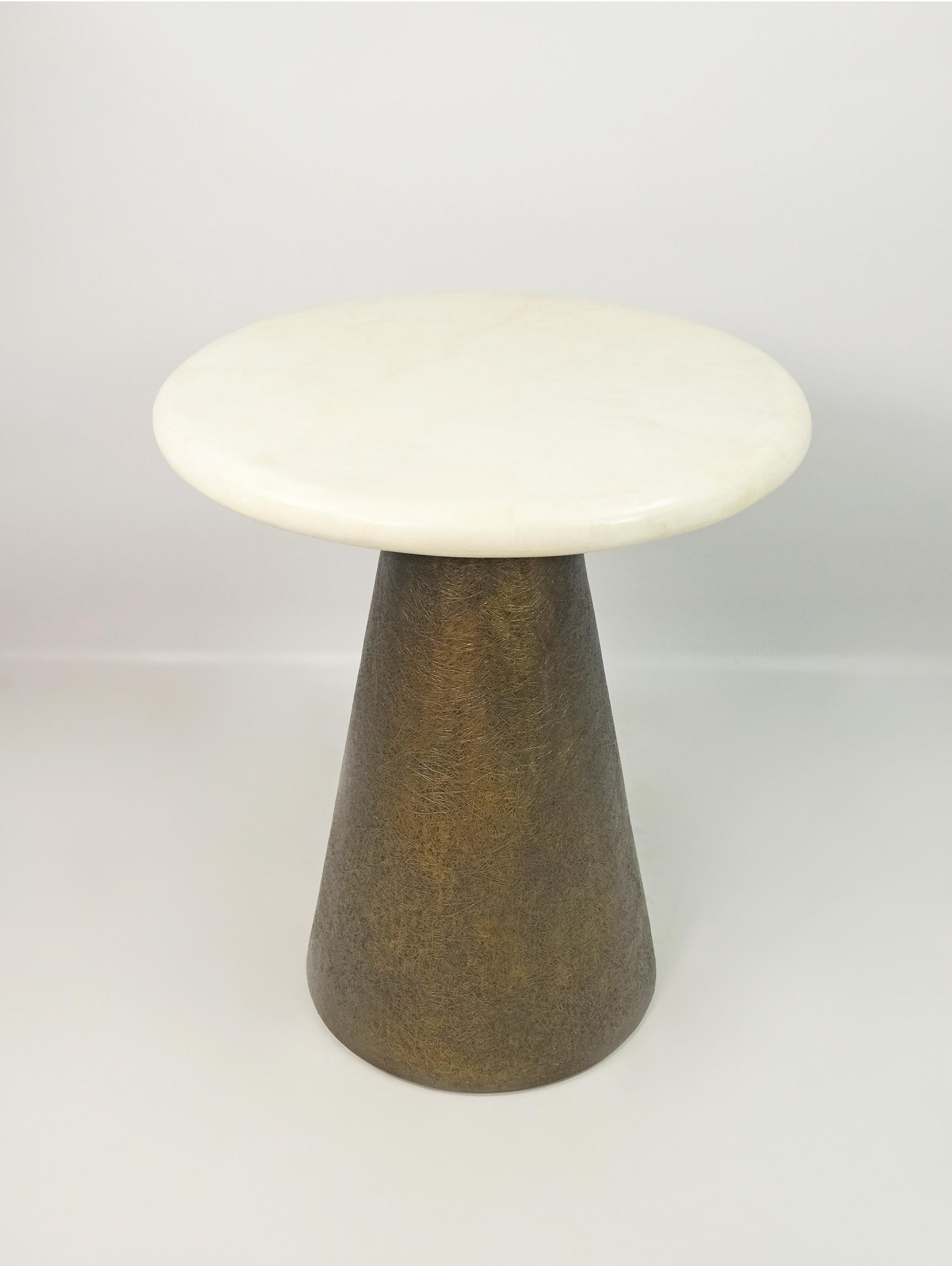 This side table is made of a round white rock crystal marquetry top.
The conical base is made of wood with a bronzed semi-raw glass fiber inlaying.
The semi raw finishing brings an interesting texture thanks to the nice rounded shape of the