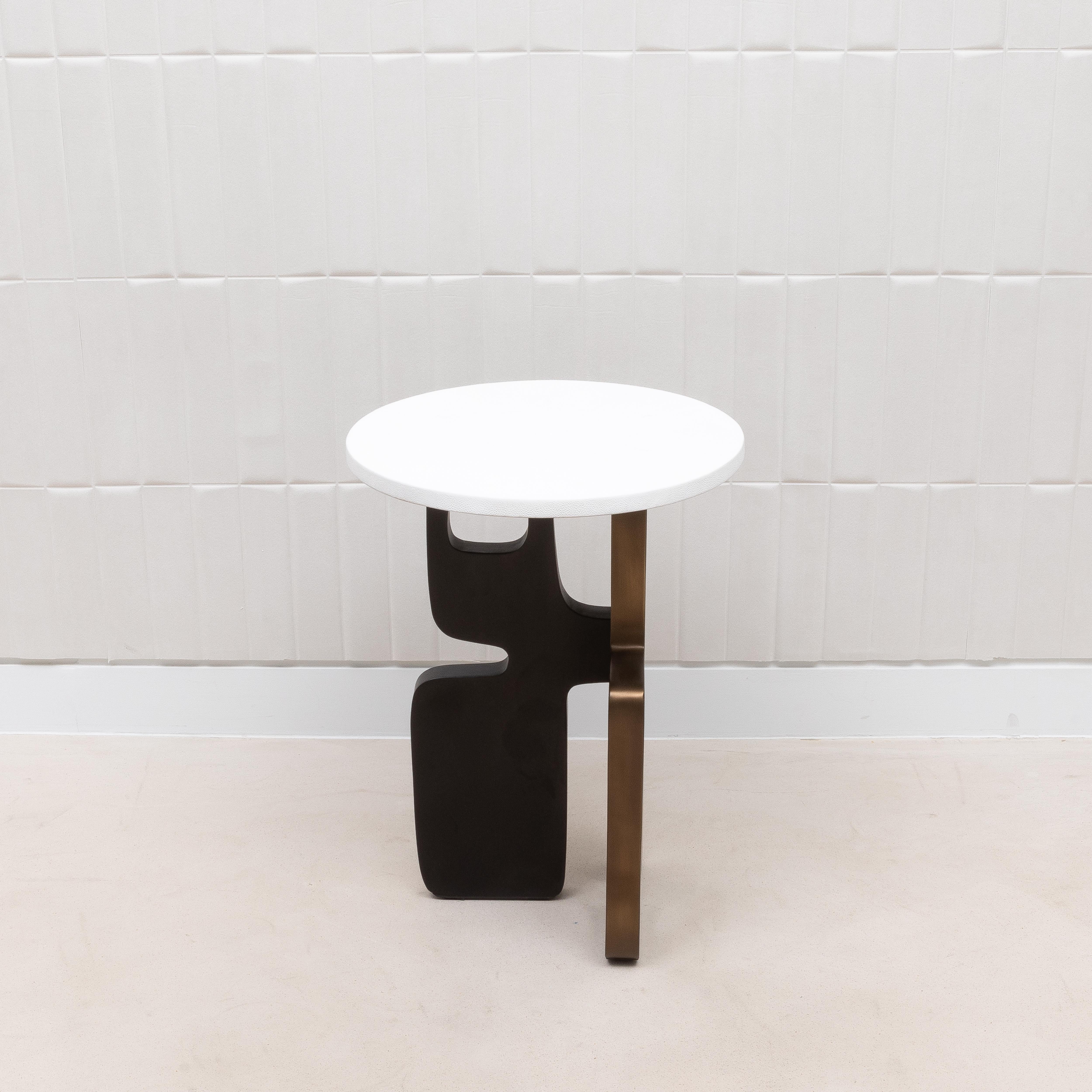 La table d'appoint Apoli de Kifu Paris est une pièce de design remarquable qui fusionne une géométrie audacieuse avec des matériaux luxueux. Son plateau, fabriqué en galuchat blanc immaculé, offre une surface élégante et sophistiquée qui est à la
