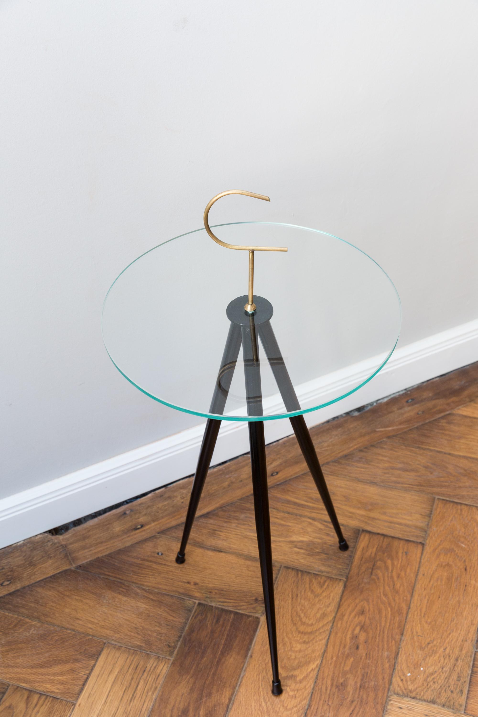 Elegant side table, Italy, circa 1950 in the style of Cesare Lacca, three black lacquered shaped metal legs, glass top, brass hook. Measures: Height 76 cm, glass plate diameter 37 cm.
Very good condition, no scratches or chips in the glass.
    