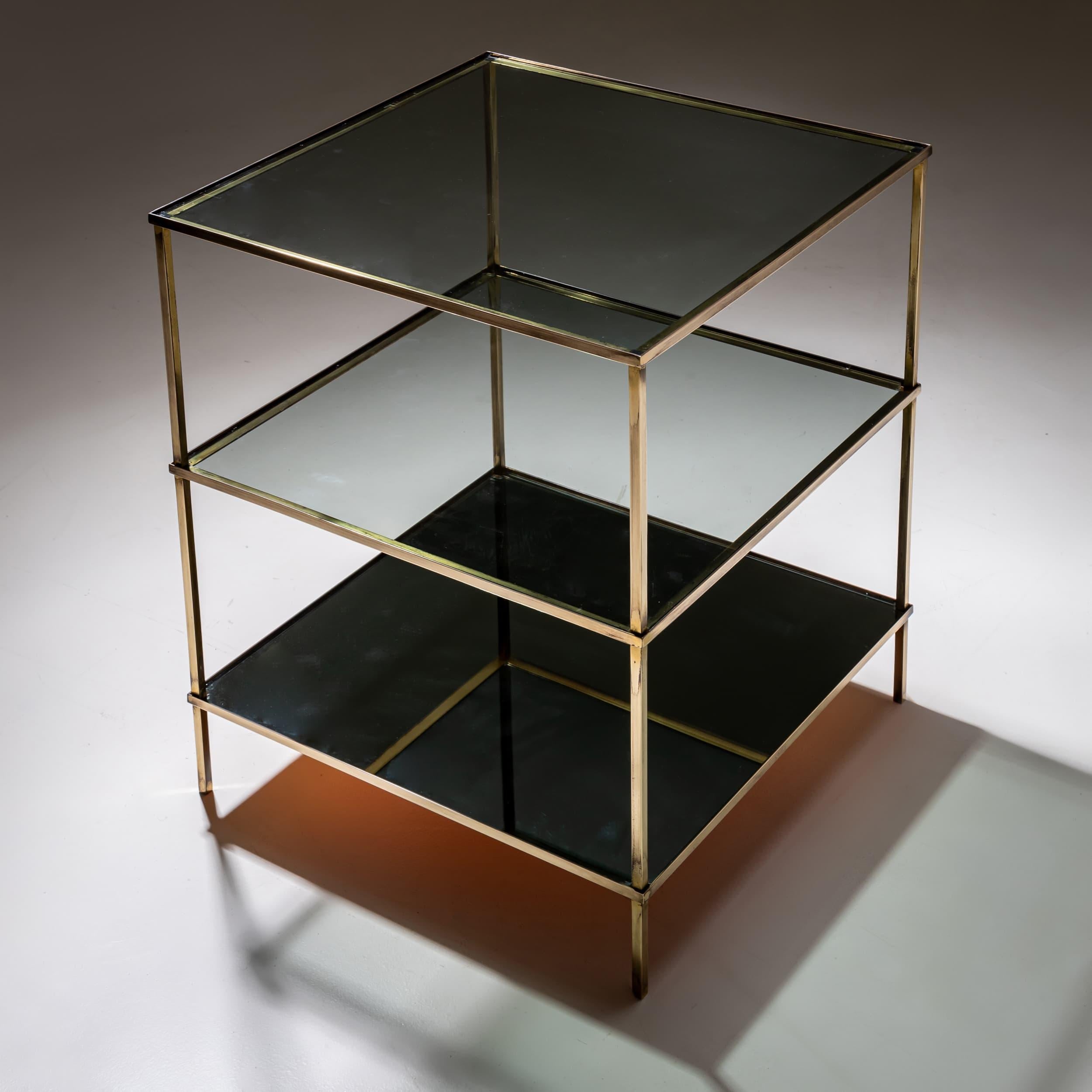 Square side table featuring three tiers and a minimalist brass frame. The top two shelves are made of dark smoked glass, while the bottom shelf is crafted from black glass. This design creates an intriguing, gradual shading effect across the glass