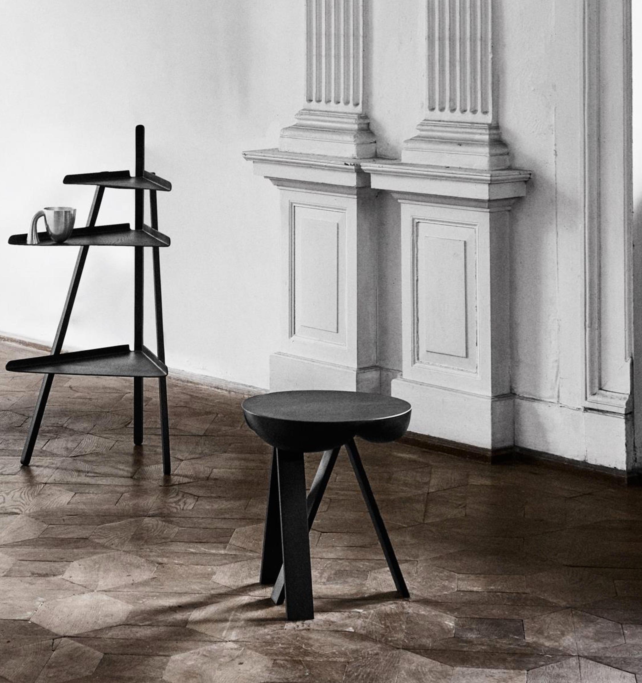 Striking. Wooden side table consisting of two stripped-down trestles and a table top. The seemingly heavy top contrasts the rigid trestles. The top gives in and provides space for the sharp ends of the trestles to lock the legs and the top together.