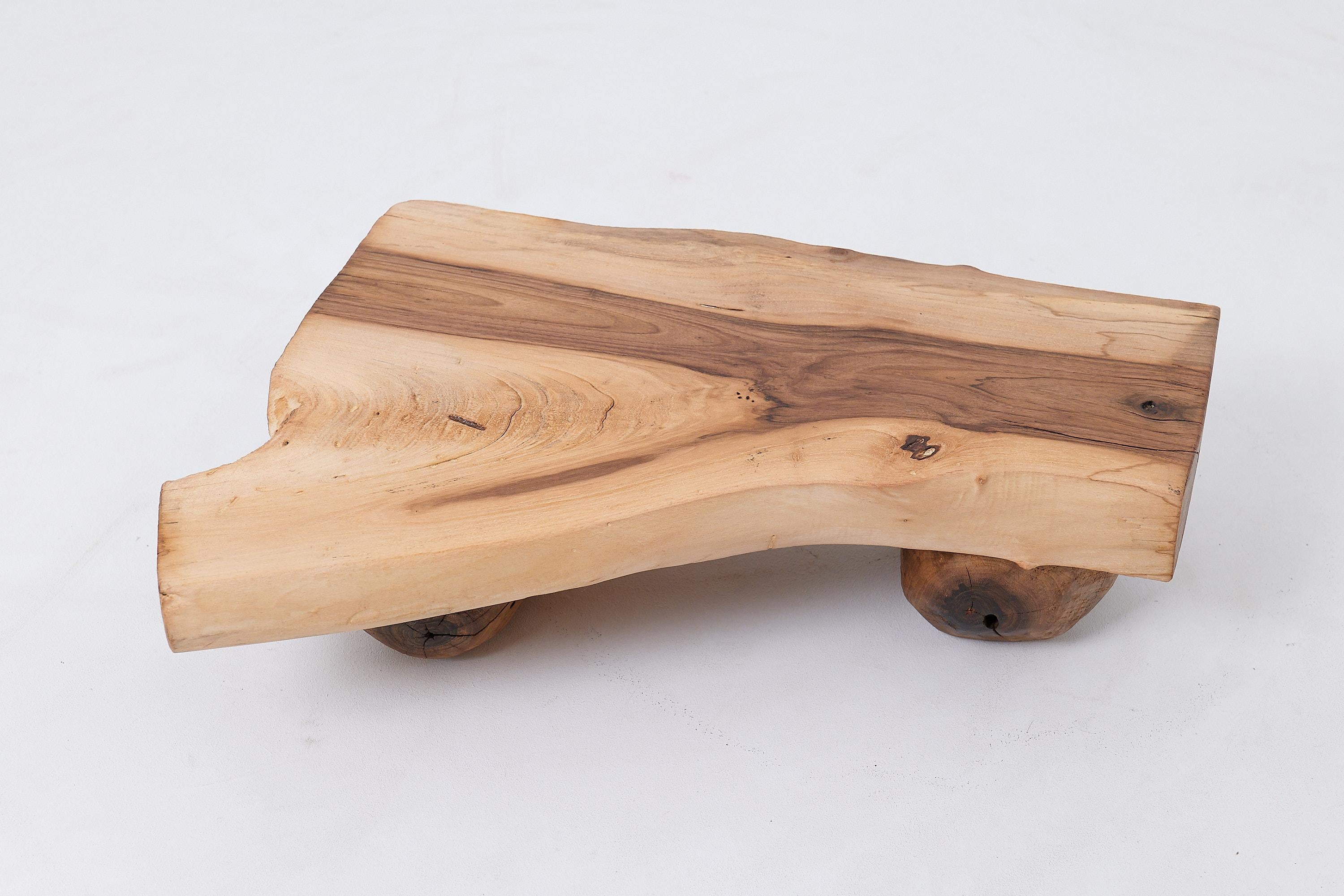 This minimalist low table is a one of a kind piece, crafted from a thick, substantial slab of solid hardwood. Its design is defined by a primitive elegance, featuring a rectangular top that rests on two sturdy, natural log supports. The form draws