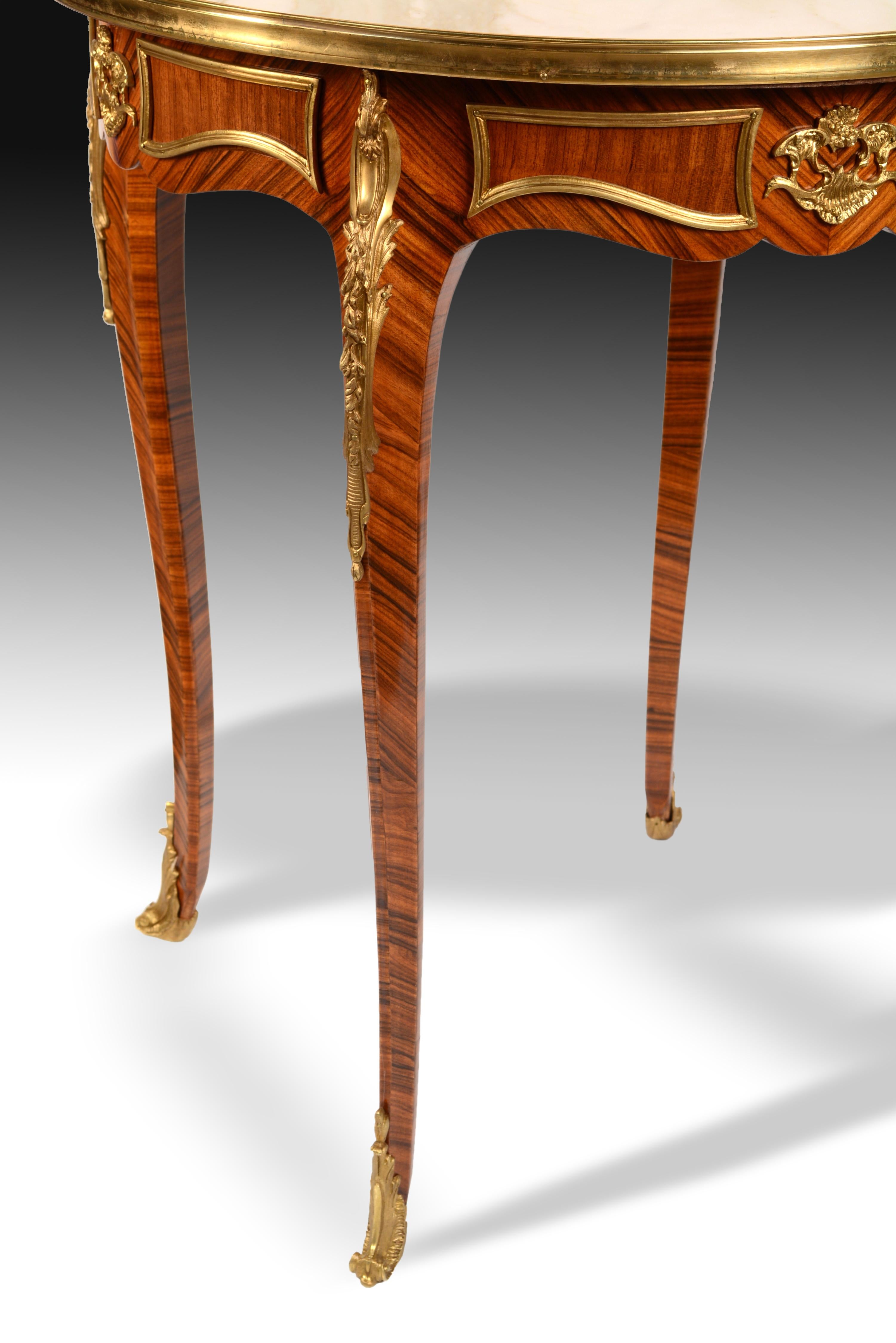 The four cabriolet legs are joined with the waist without visual separation to highlight the wood of rosewood, which has also been used in plates on the fronts of the table changing the arrangement of the veins. The decorations in gilded metal