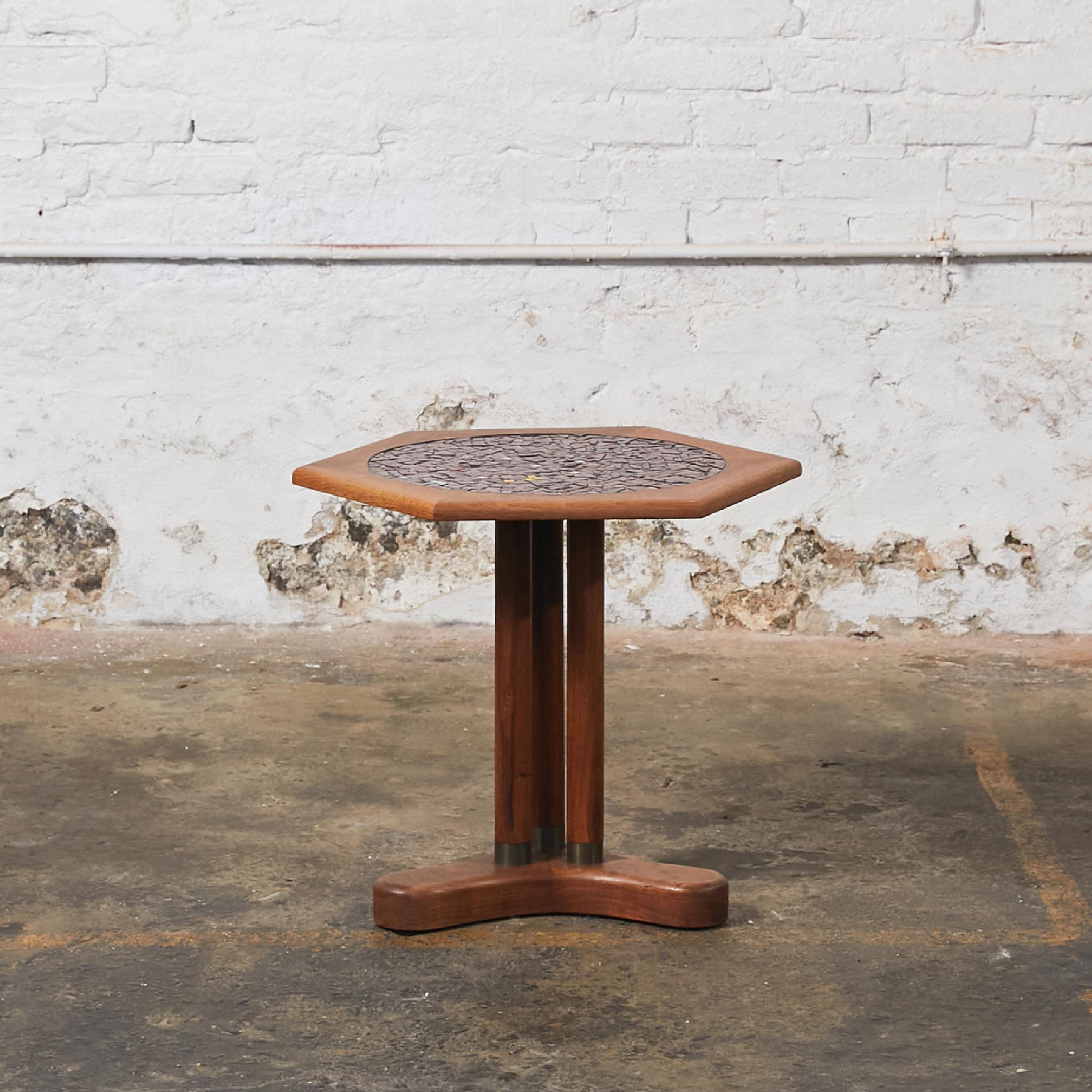 Hexagonal midcentury side table in the style of Gordon & Jane Martz. The table top is inlaid in glass mosaic in different shades of dusty pink, with sparks of yellows and blacks. The top sits on three cylindrical legs with bronze end, resting on