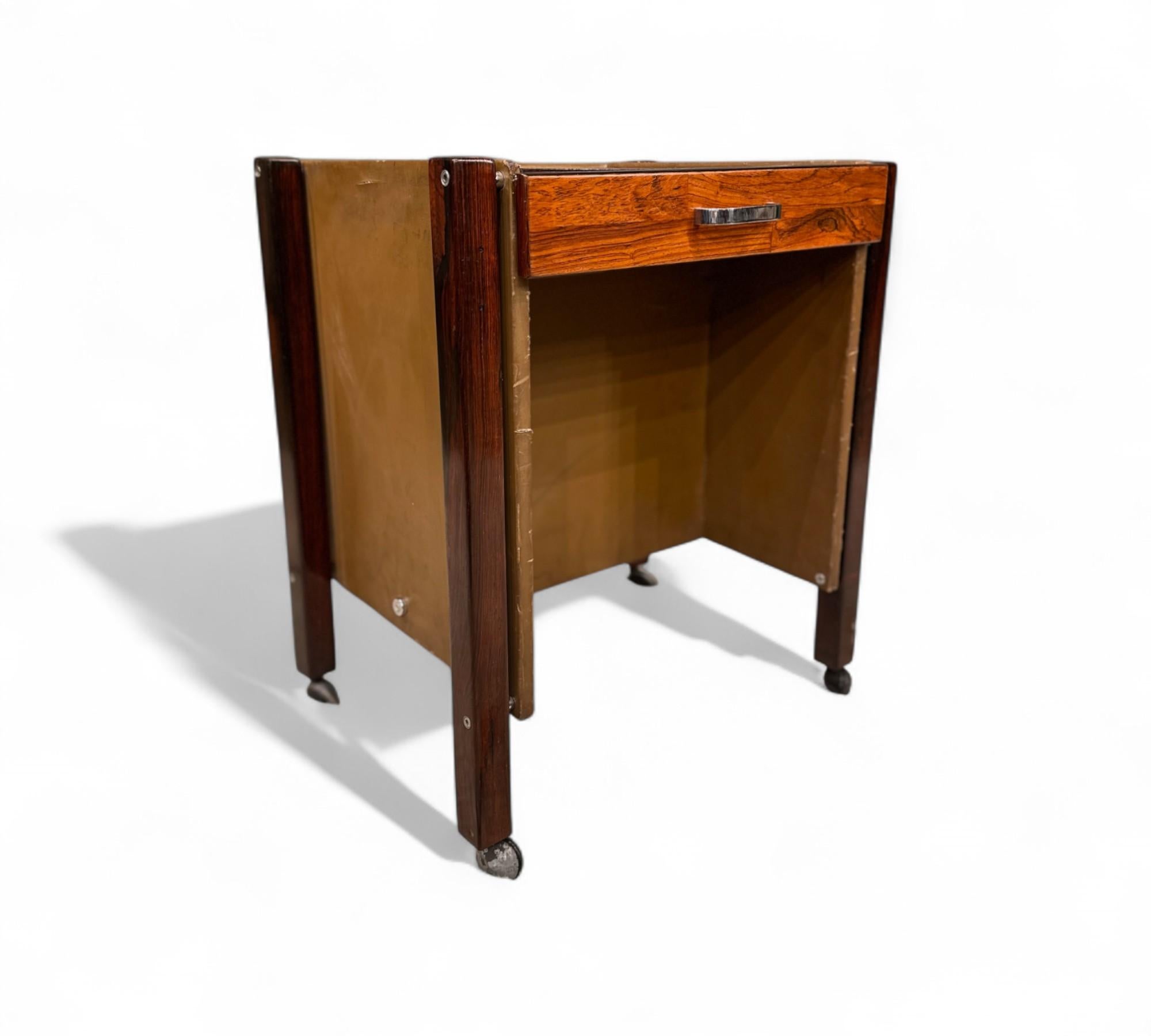 Cette table d'appoint est magnifiquement fabriquée en bois dur et finie avec un placage en bois dur brésilien. Il comprend un seul tiroir pour un rangement pratique et repose sur quatre pieds équipés de roues chromées pour une mobilité aisée. Les