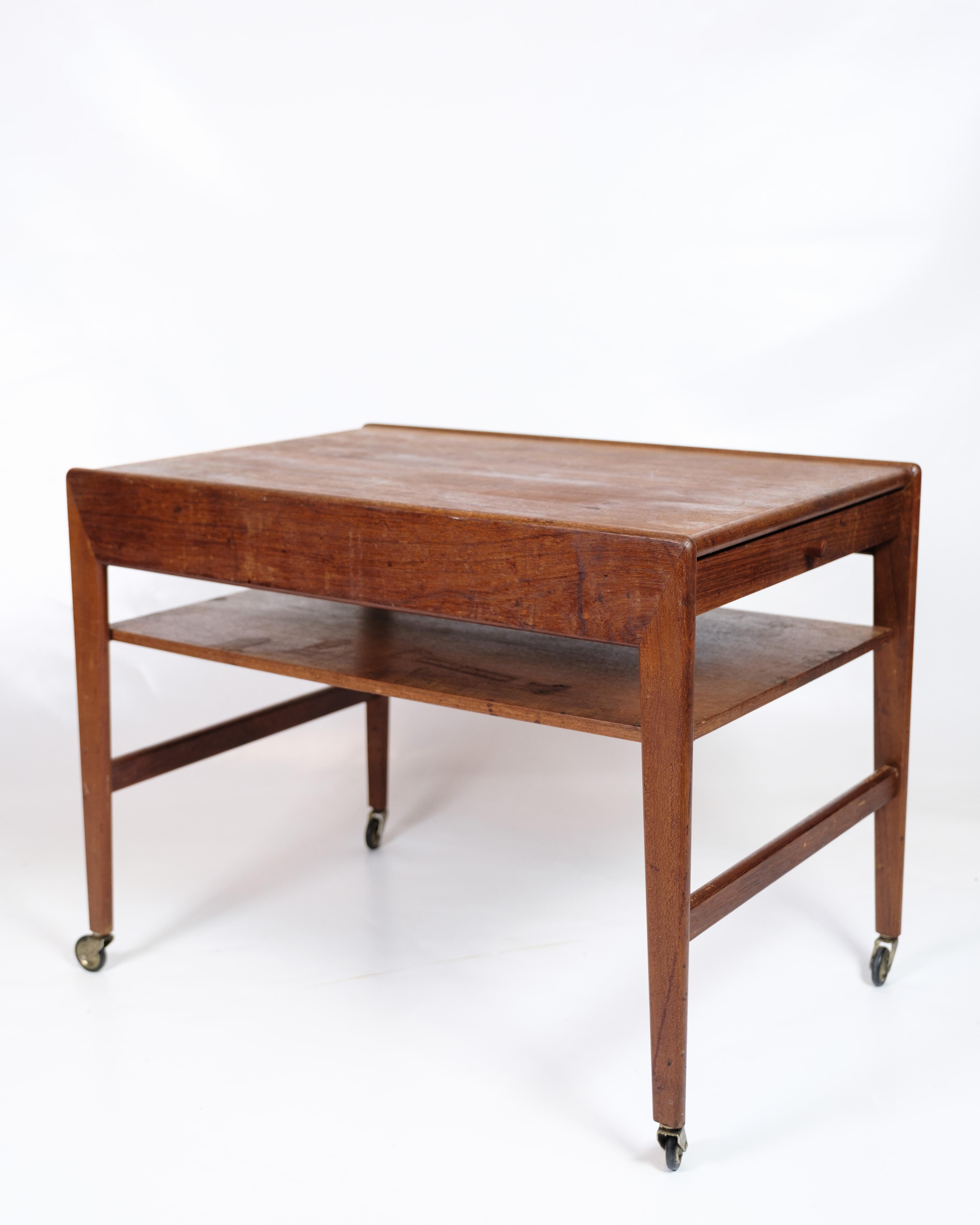 Teak side table from the 1960s, made in Danish design. The table is mounted on wheels, making it easy to move around, and has both built-in drawers and a small shelf, which provides practical storage space. The design combines functionality and