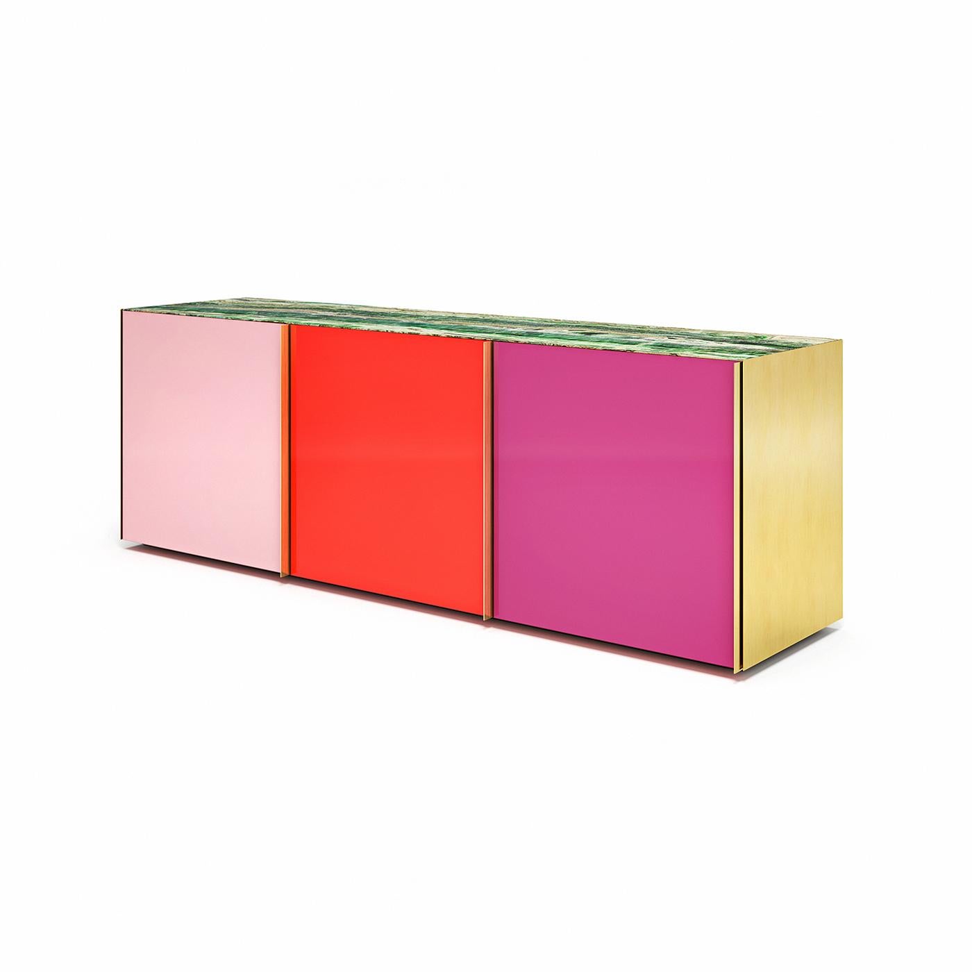 This eye-catching sideboard stands out for its vibrant colors and mesmerizing reflections. Its silhouette comprises a lacquered wooden structure equipped with three glass shelves, framed by side brass panels, and closed on the front by three glass