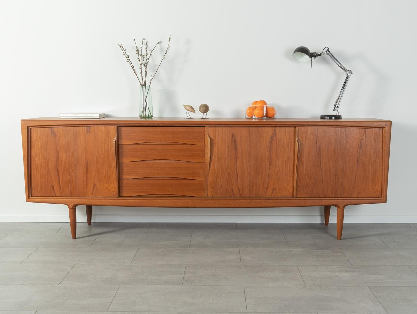 Filigree sideboard by Omann Jun., model 18. High-quality corpus in teak veneer with two sliding doors, an insert shelf, four drawers and cigar shaped feet.
Quality Features:

 Accomplished design: perfect proportions and visible attention to