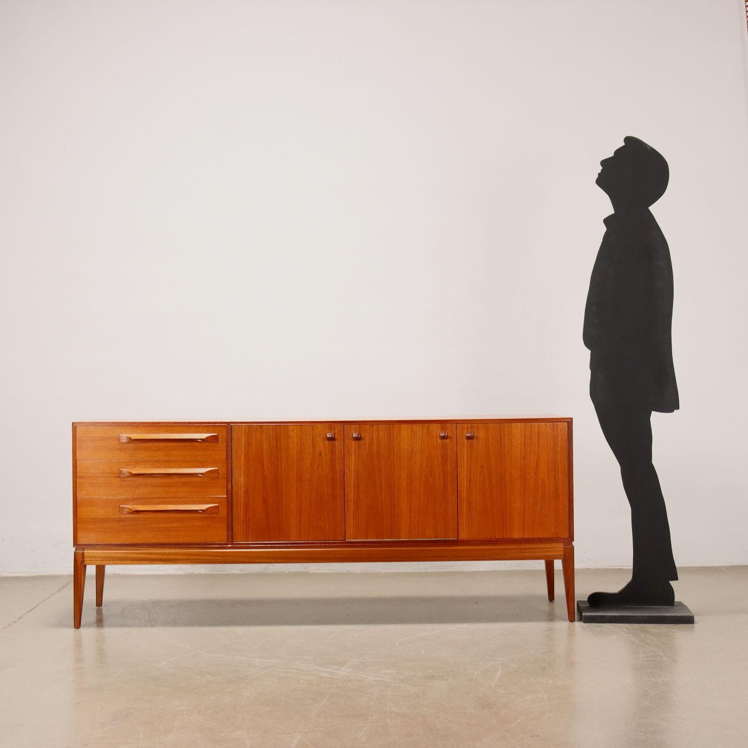 Sideboard vintage di manifattura inglese in legno impiallacciato teak con tre cassetti, due ante a battente, una a ribalta con piccolo piano estraibile. Restaurato nei nostri laboratori, presenta il marchio della produzione.