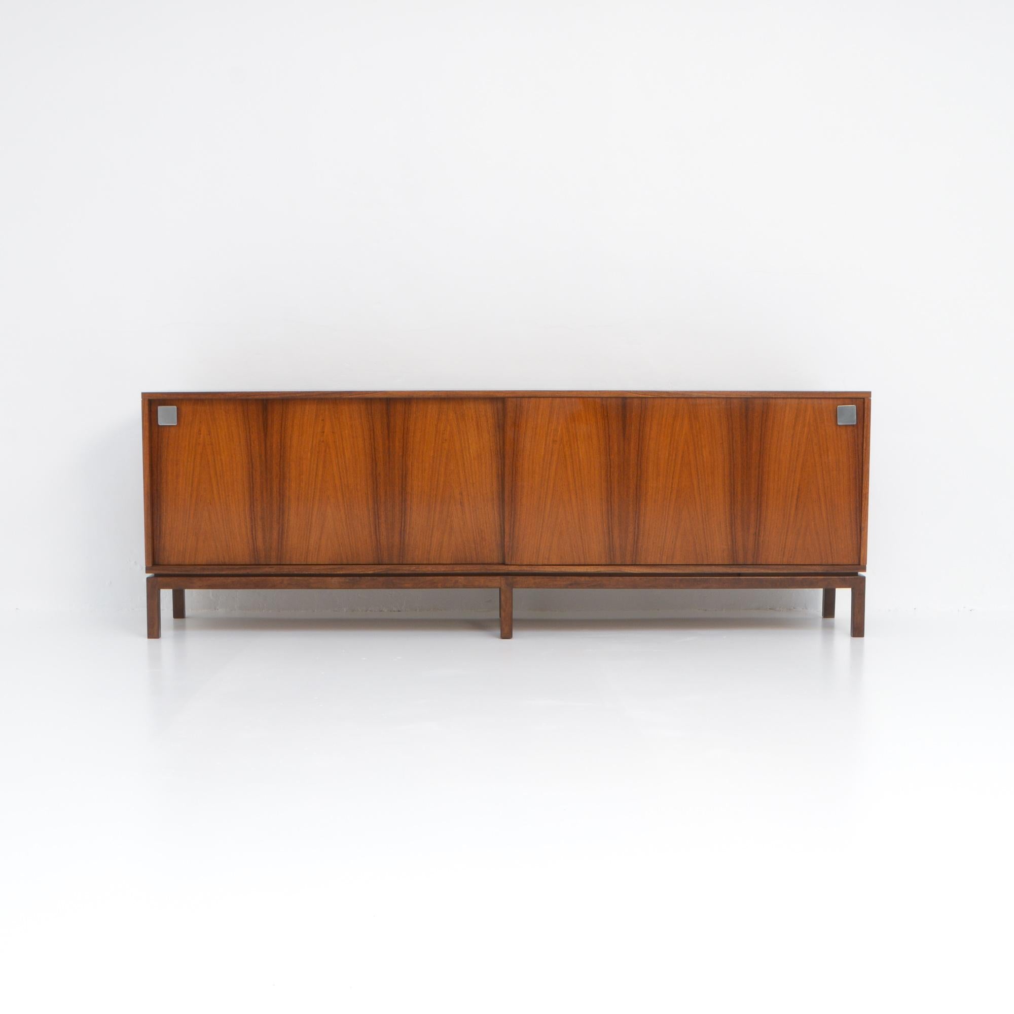 This beautiful sideboard was designed by Alfred Hendrickx in the 1960s.
It is a pure design and a high quality piece of furniture.
The pattern of the wood veneer of the 2 sliding doors is amazing and creates a dynamic effect, the sleek wooden base
