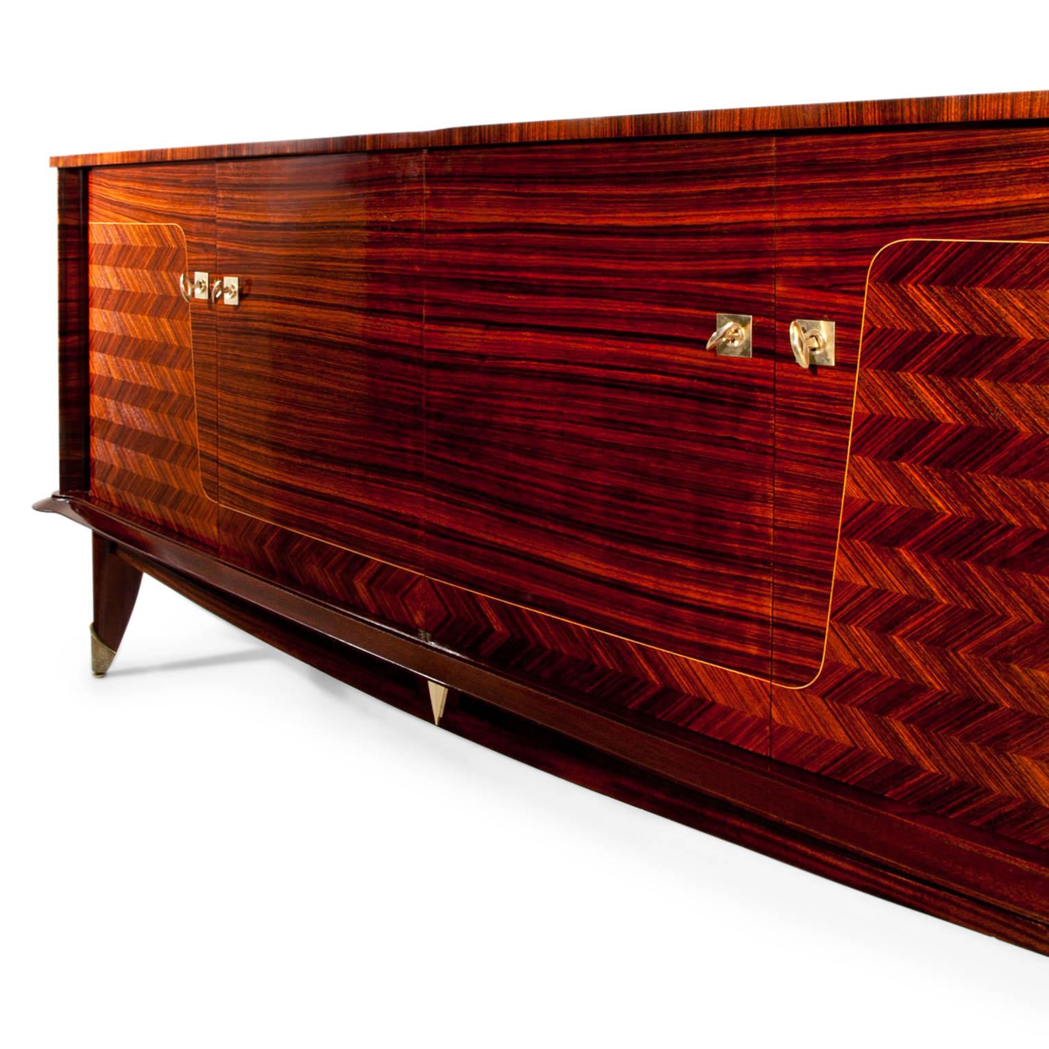 Long sideboard with four doors, standing on tapered feet with brass caps. At the front and on top crisscross patterned veneer as well as a horizontal veneer pattern that is separated with a thin thread inlay. The interior is in maple and has shelves