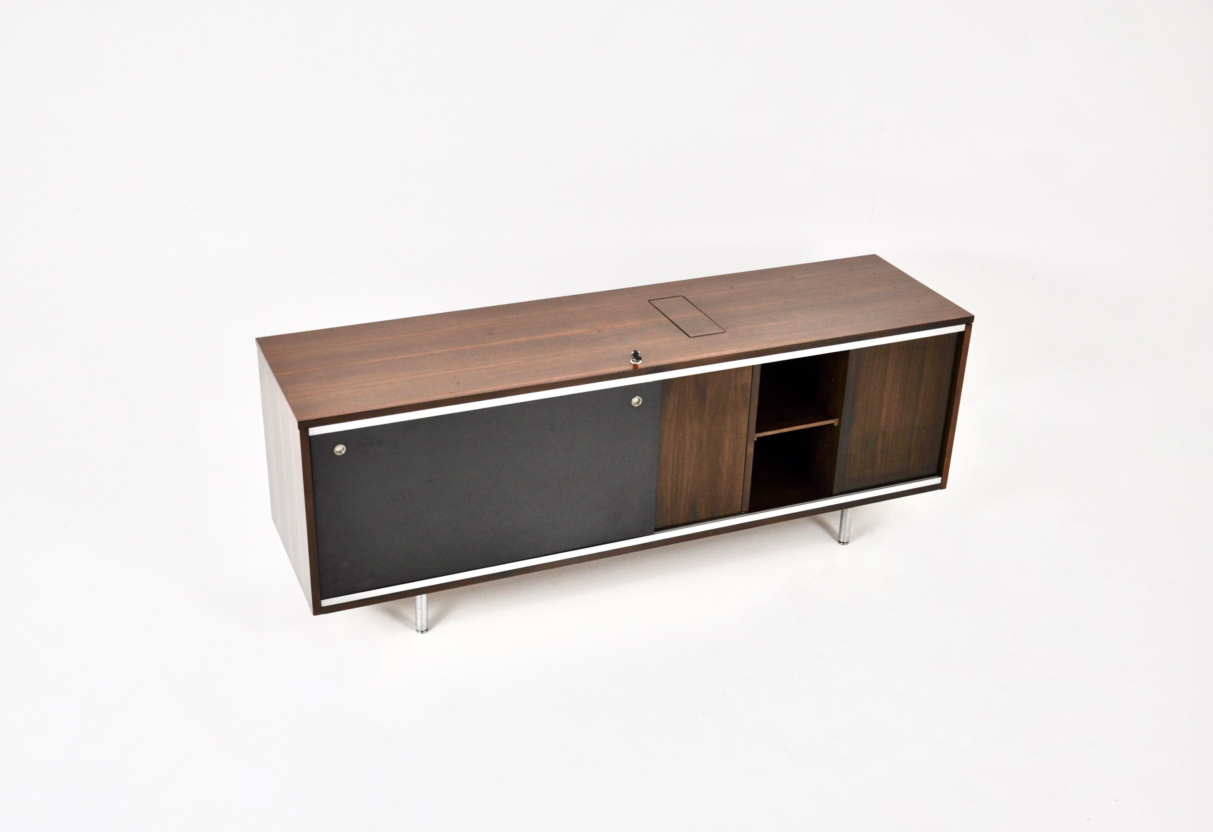 Aparador de madera con 1 puerta corredera negra que contiene dos estantes regulables en altura. Hay una puerta en el lateral que contiene un estante, y una trampilla en la parte superior para poder colocar una papelera dentro del mueble. Las puertas