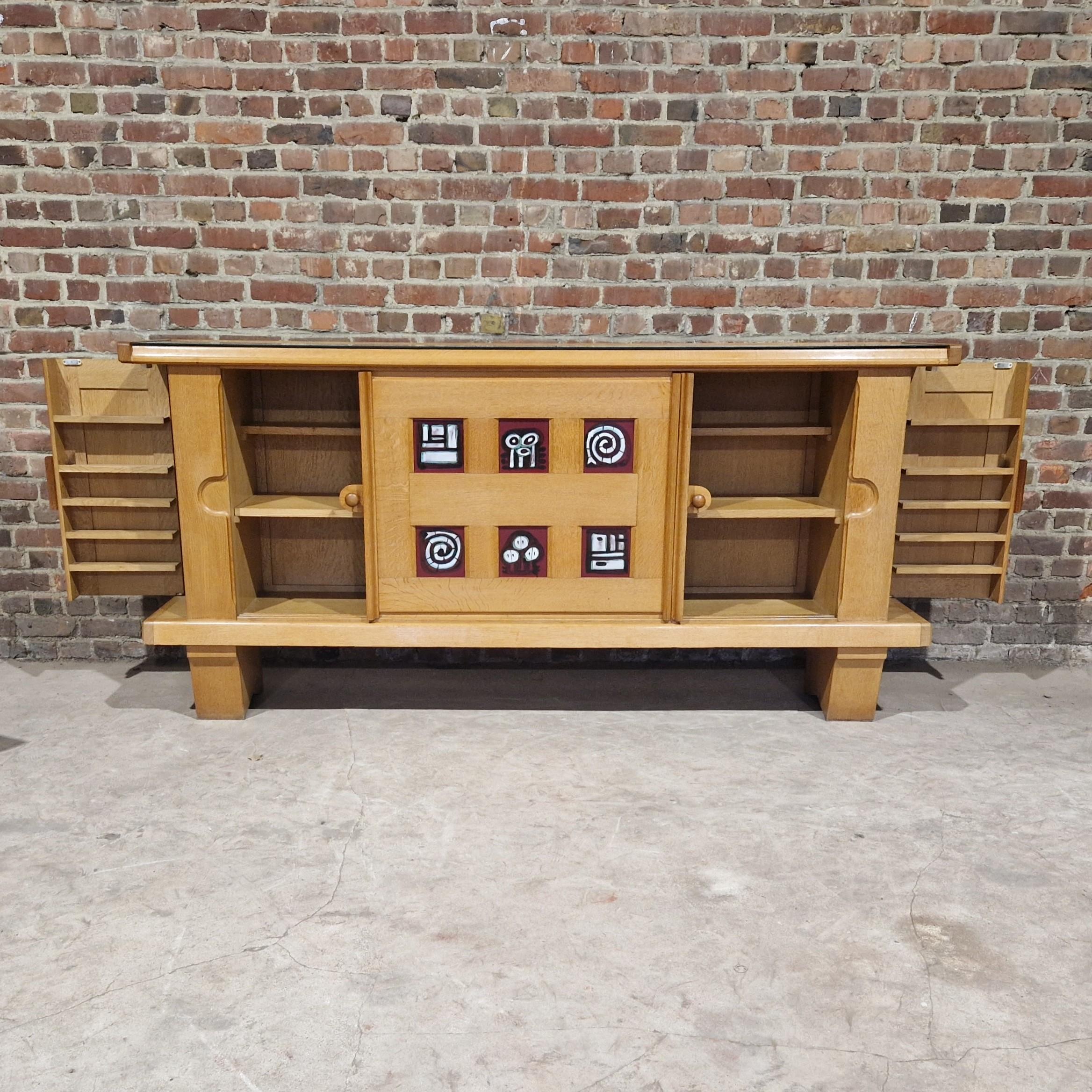 Large vintage sideboard in light oak, Guillerme and Chambron, ceramics by Danikovski. It opens with two sliding doors revealing large storage spaces and two hinged side doors forming a glass panel. The top is protected by a thick slab of glass.