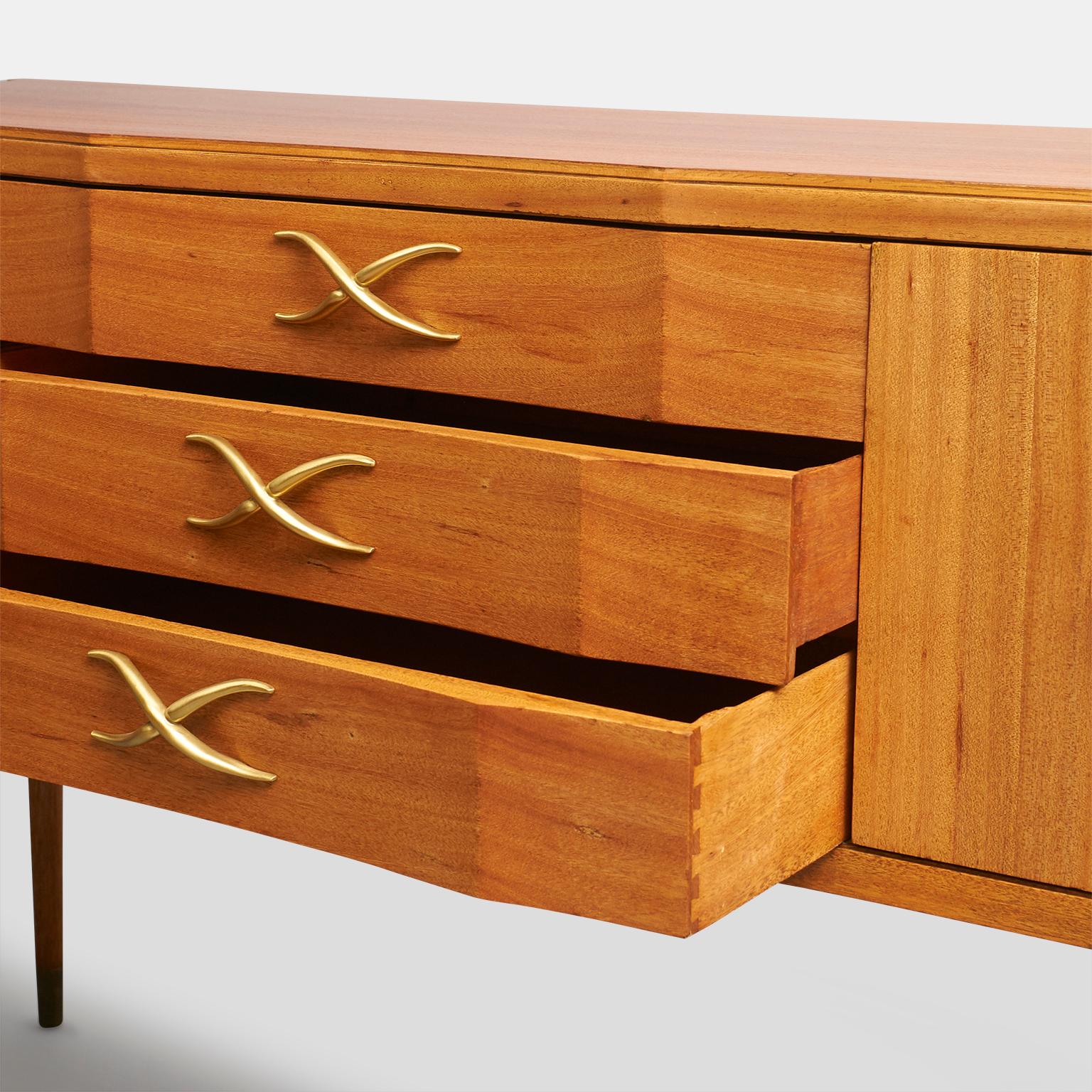 A sideboard or buffet by Paul Frankl in bleached mahogany with Brass “X” from handles on the three drawers and brass ring pulls on the two doors.