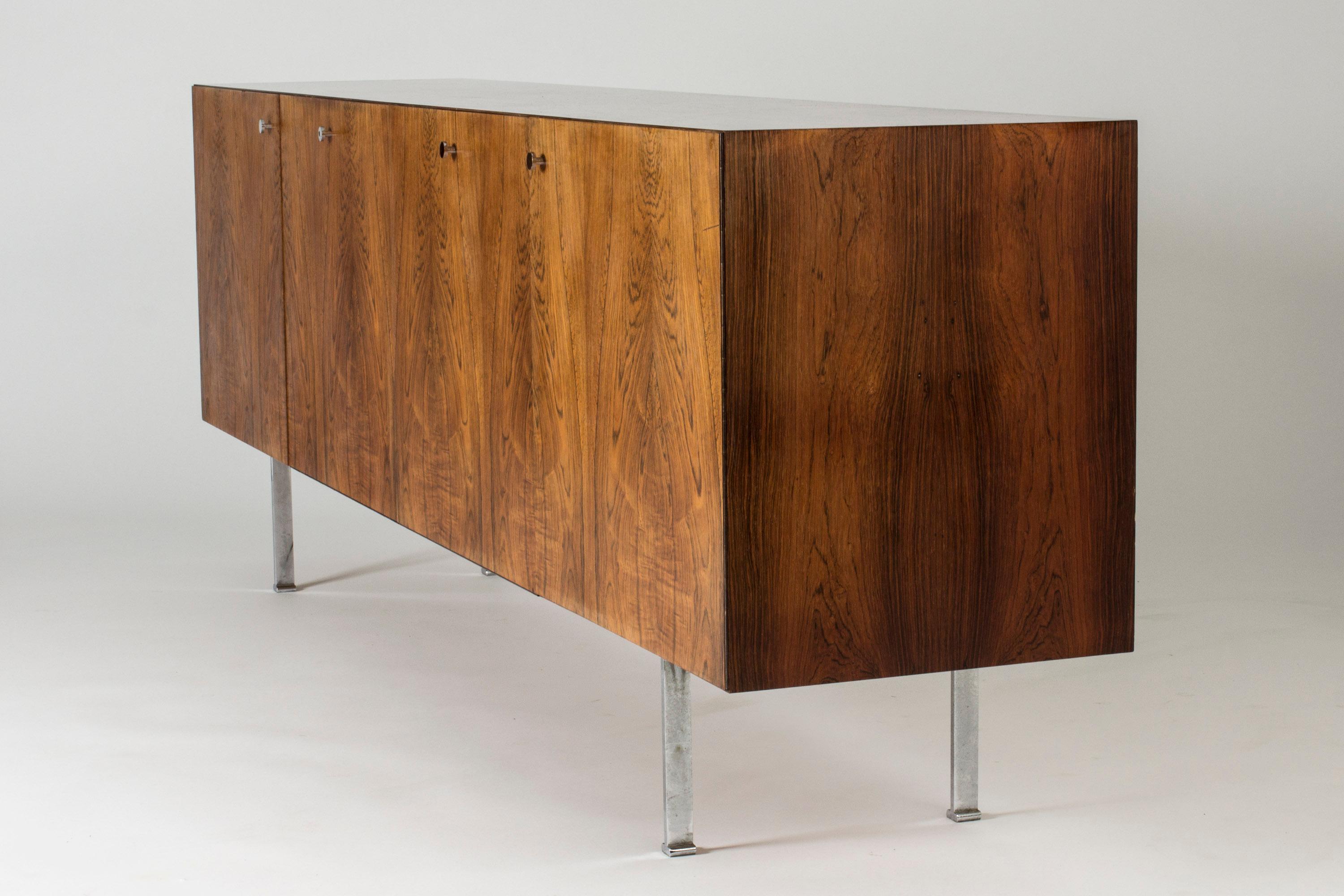 Striking rosewood sideboard by Poul Nørreklit, in a sleek design with beautiful, flaming woodgrain on the door fronts. Sleek steel legs and handles. Bar section inside with white glass shelves.