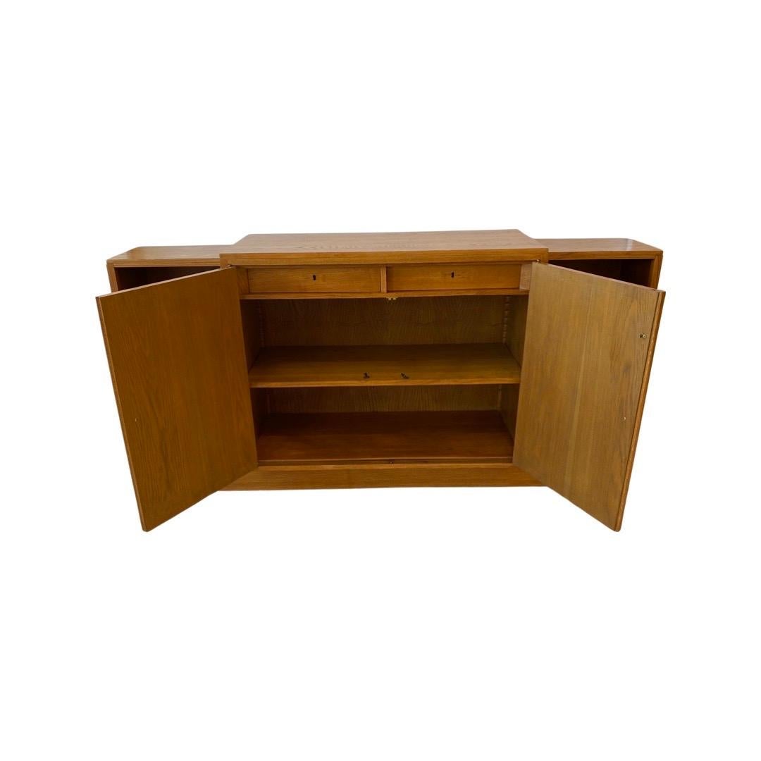 A Stained Oak Cabinet that features 2 doors concealing 2 locking drawers and one adjustable shelf.  There are Shelves on each side of the cabinet. This piece came from La Cité Universitaire de Paris and it was designed by Jacques Émile
