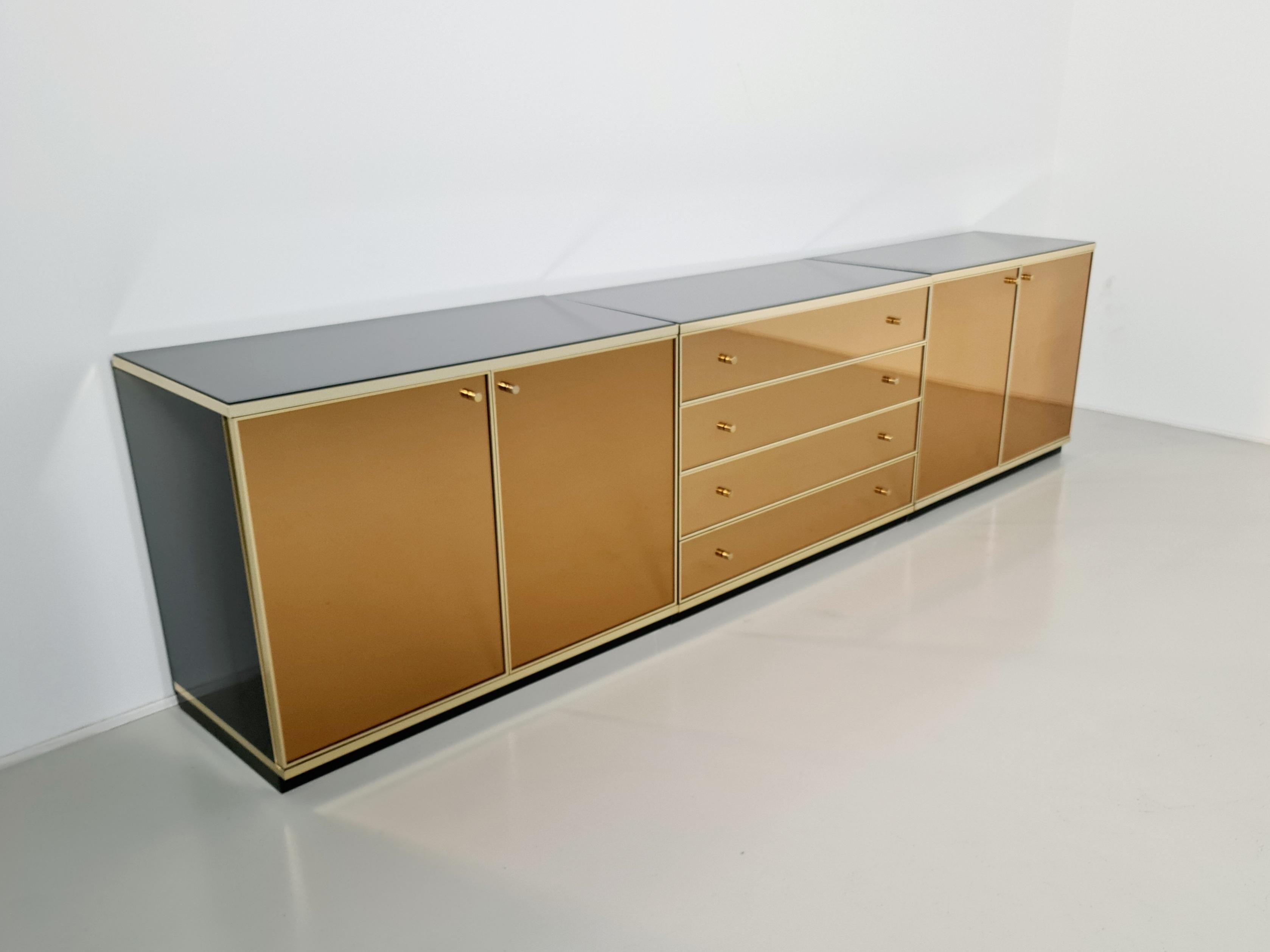 Sideboards by Renato Zevi. Brass and pink goldish smoke mirror faces, black opal glass top and brass details. Can also be seperated to make a smaller sideboard and a chest of drawers. Famous design like Willy Rizzo, Mario Sabot, Guy Lefèvre, Mahey,