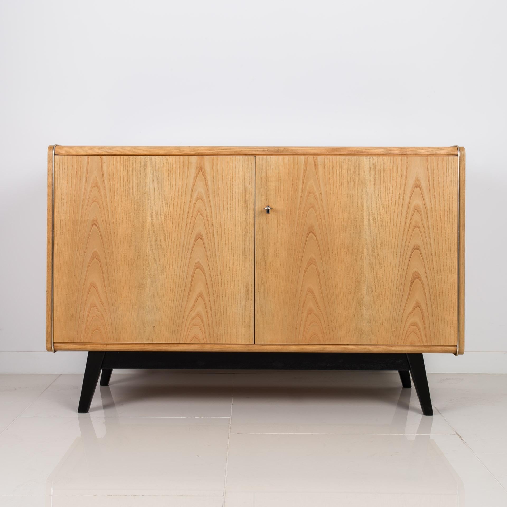 This sideboard was designed by Bohumil Landsman and produced by Czech company JITONA in 1960s. The piece is in very good original condition, veneered with ash. Original label preserved on the back. The top is covered with black opaxite glass. Inside