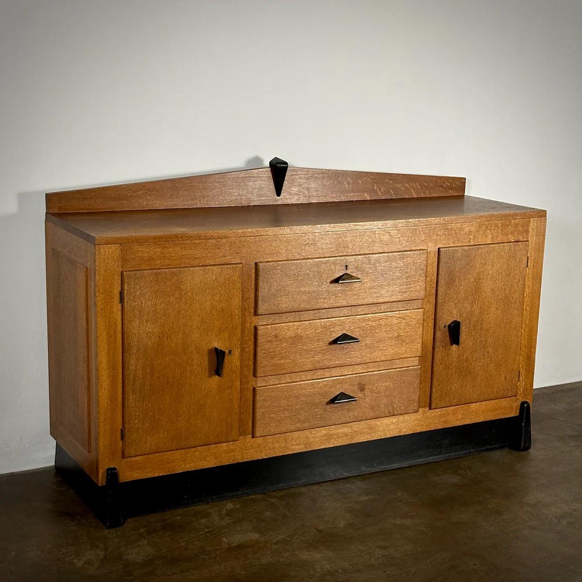 Dutch Amsterdam School sideboard crafted in oak, distinguished by unique metal handles and an Art Deco frieze. This piece features three central drawers flanked by spacious cupboards, combining traditional craftsmanship with the bold, expressionist