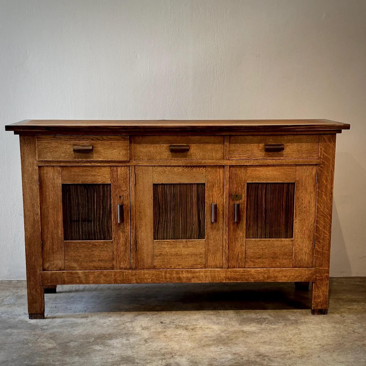 Amsterdam school sideboard in oak with paneled cupboards and raised handles in wenge wood. This piece exemplifies early 1900s Dutch design, blending utility and aesthetics. It's perfectly suited as either a credenza or a bar cabinet, offering