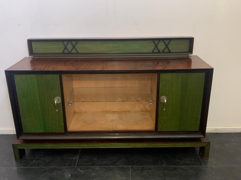 Rosewood veneered body on the front flared frame in solid rosewood welcomes central decorated glass and maple side doors finished with green aniline. Futurist-style handles are made of satin silver-coloured metal. All supported by a linear base,