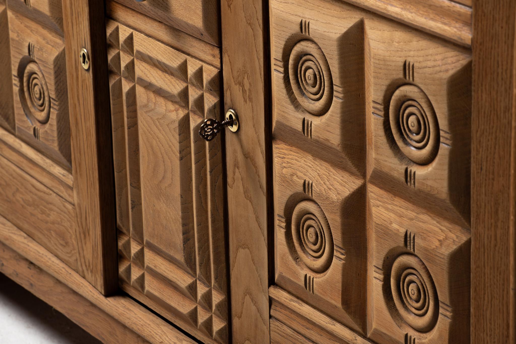 Una facciata di geometrie ritmiche e rilievi tattili, questa credenza francese degli anni '60 si afferma sia come mobile che come scultura. I suoi ornamenti intagliati - ipnotici medaglioni a occhio di bue e motivi piramidali a gradini - emergono