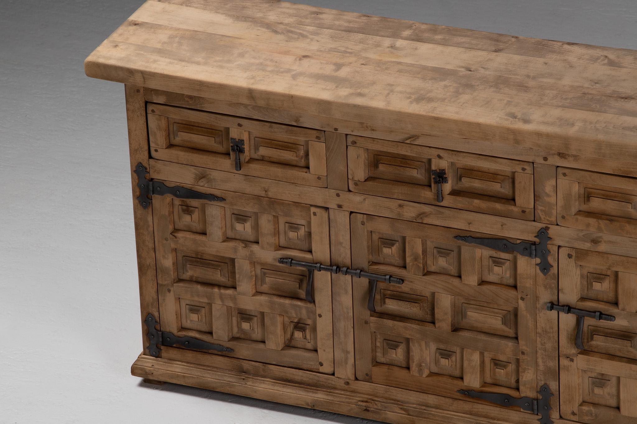 Severe yet elegant, this Spanish buffet from the 1950s asserts a bold, architectural presence—its façade carved in a rhythmic grid of relief panels, each block subtly irregular, like hand-hewn stone. More fortress than furnishing, the composition