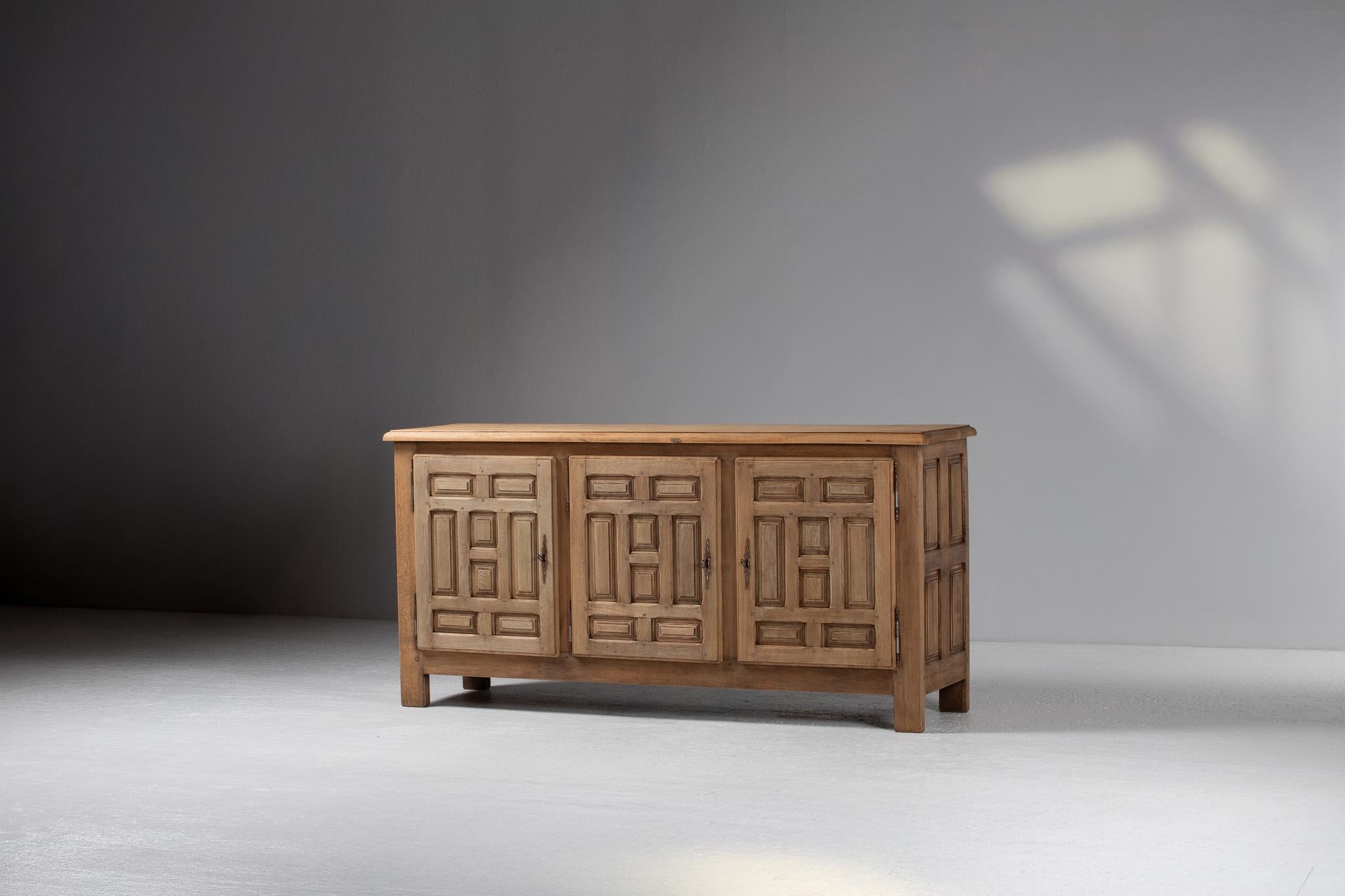 With the solemnity of an ancestral wall and the quiet poise of light brushing against stone, this Spanish sideboard expresses a tectonic language of austere form and architectural rhythm. Its tripartite front, composed of deeply framed geometric