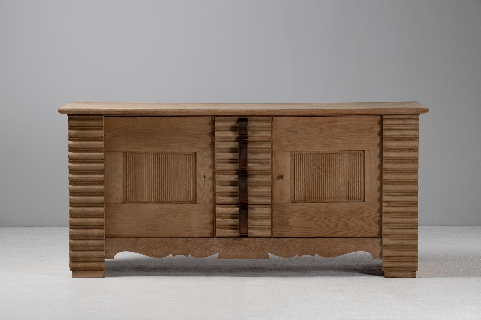 The façade of this sideboard pulses with an almost rhythmic solemnity—deeply fluted pilasters catch the light in alternating ribbons of shadow, while the sculpted iron pulls arc like calligraphic strokes across the vertical grain. At once austere