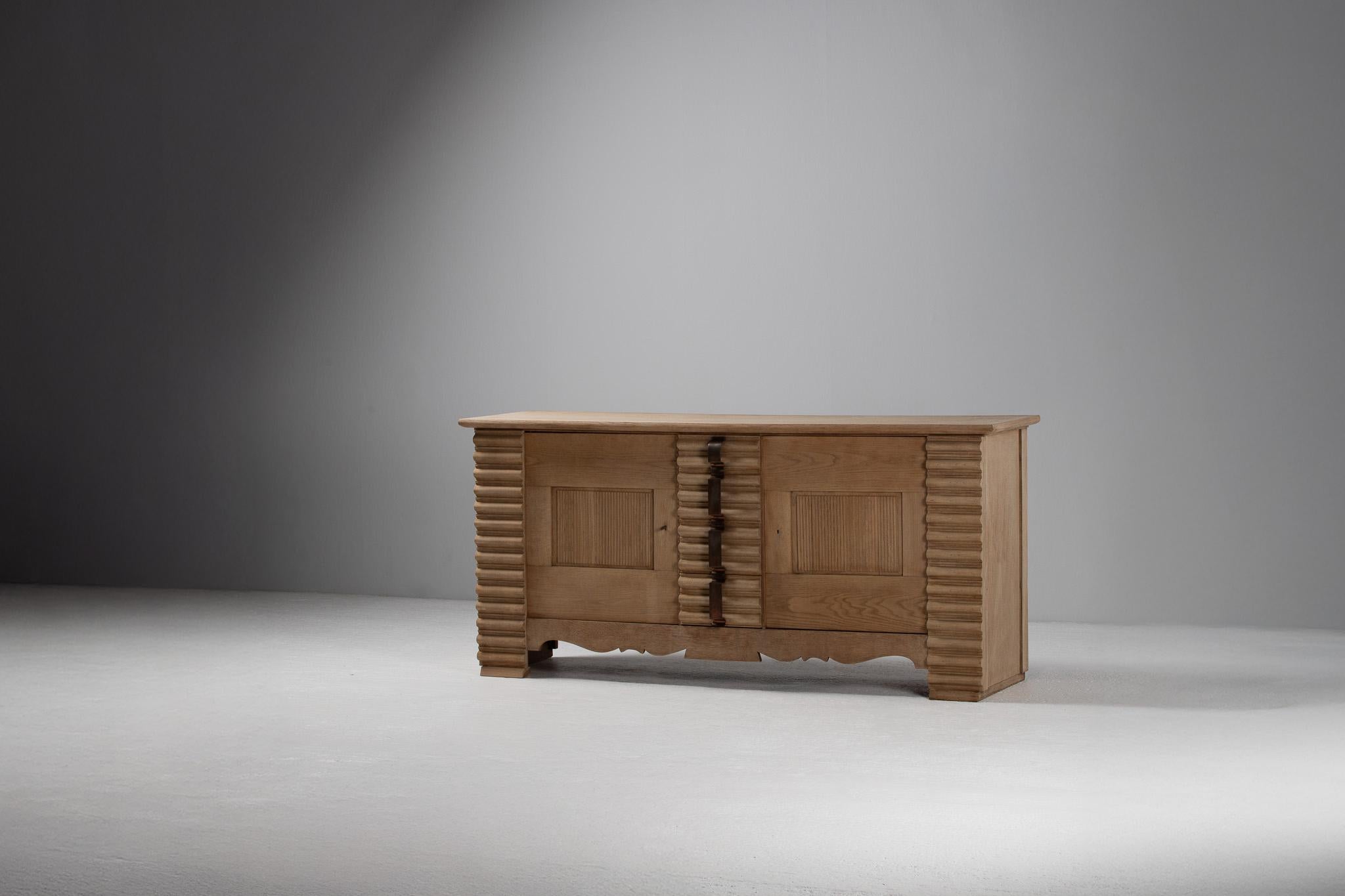 The façade of this sideboard pulses with an almost rhythmic solemnity—deeply fluted pilasters catch the light in alternating ribbons of shadow, while the sculpted iron pulls arc like calligraphic strokes across the vertical grain. At once austere