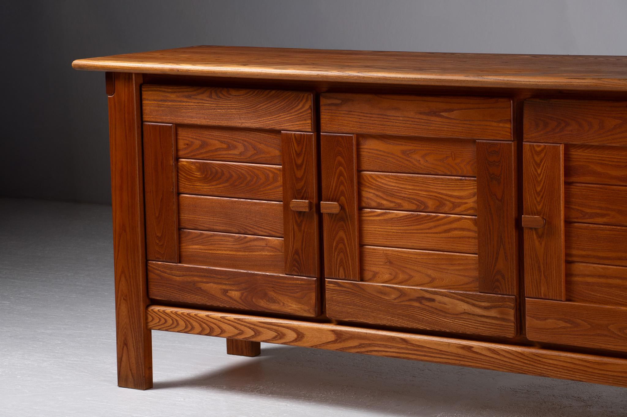 Buffet en orme massif, France, 1970

Avec son articulation horizontale et son allure architecturale sereine, ce buffet évoque la force tranquille du modernisme rural. La silhouette est élémentaire - un monolithe adouci par sa patine chaude et dorée
