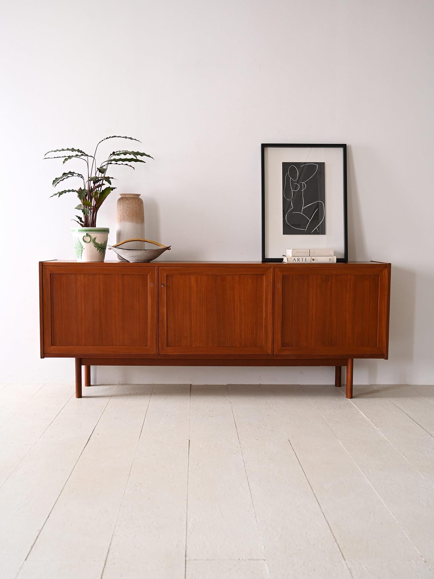 Scandinavian teak sideboard original vintage 1960s.

Featuring a simple structure with square, modern lines, this piece embodies the spirit of Nordic design of the era. Made of fine teak wood, the sideboard exudes warmth and sophistication while the