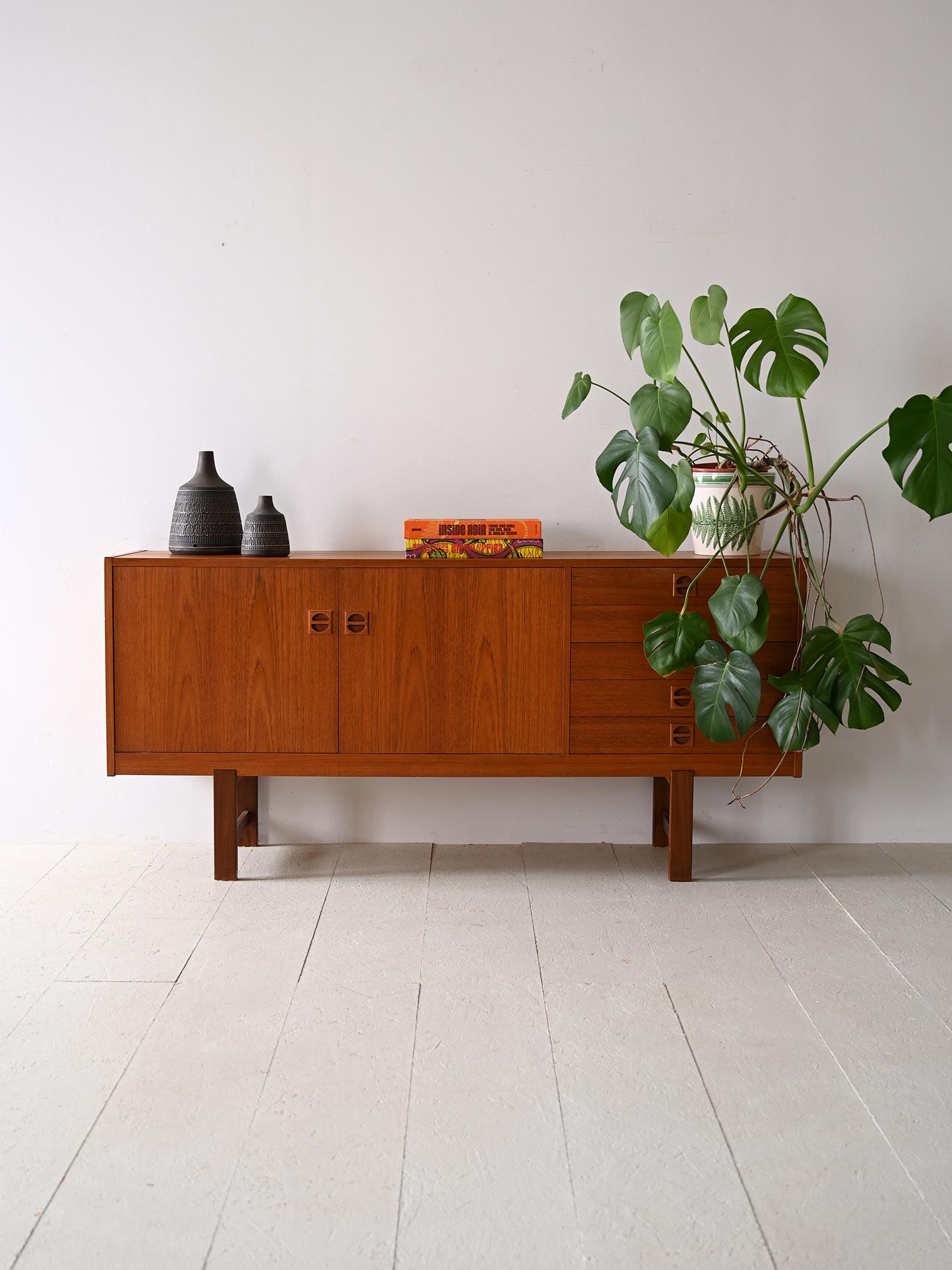 Scandinavian 1960s teak sideboard. A piece of original modernism with timeless style. The simple, straightforward structure features a storage compartment closed by two hinged doors on one side and five drawers on the other. The carved wooden handle