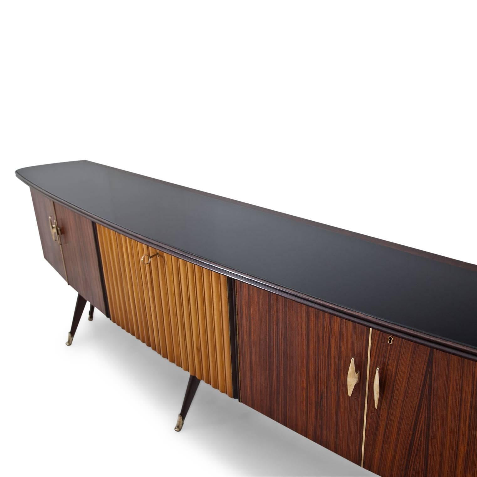 Long sideboard standing on thin legs with brass sabots and a slightly curved front. The sideboard has three compartments with double doors, the middle doors are structured with vertical groves. The sideboard was professionally refurbished.