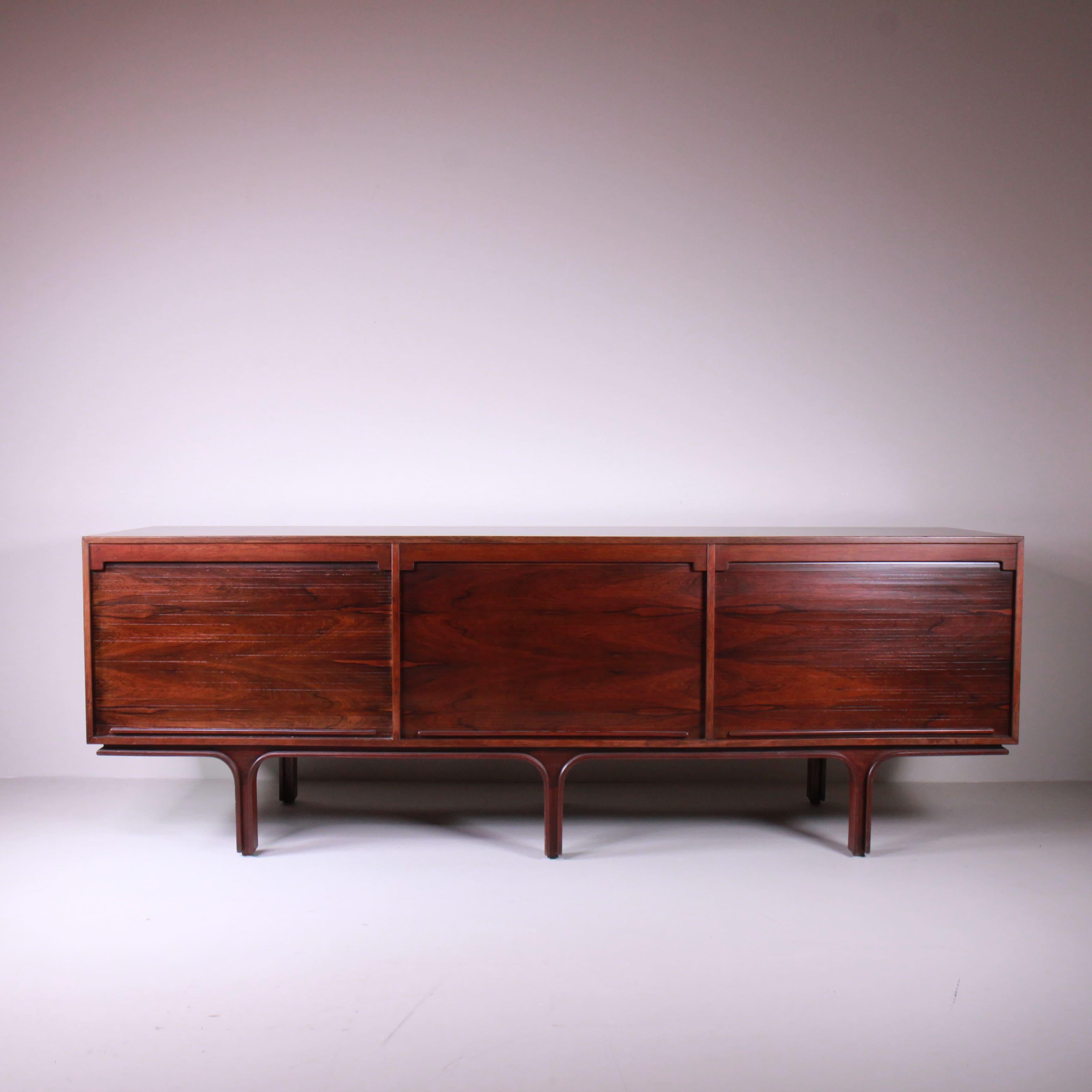 The M501 Credenza, designed by Gianfranco Frattini for Bernini in 1960, is a symbol of elegance and functionality. This extraordinary piece, made of rosewood, is characterized by its sliding shutters that conceal the interior compartments while